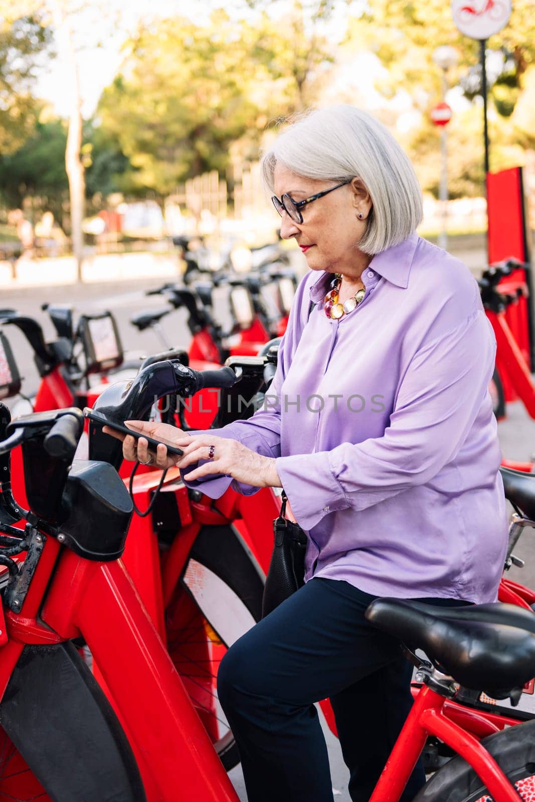 senior woman unlocking rental bike with the app on her mobile phone, concept of sustainable mobility and active lifestyle in elderly people