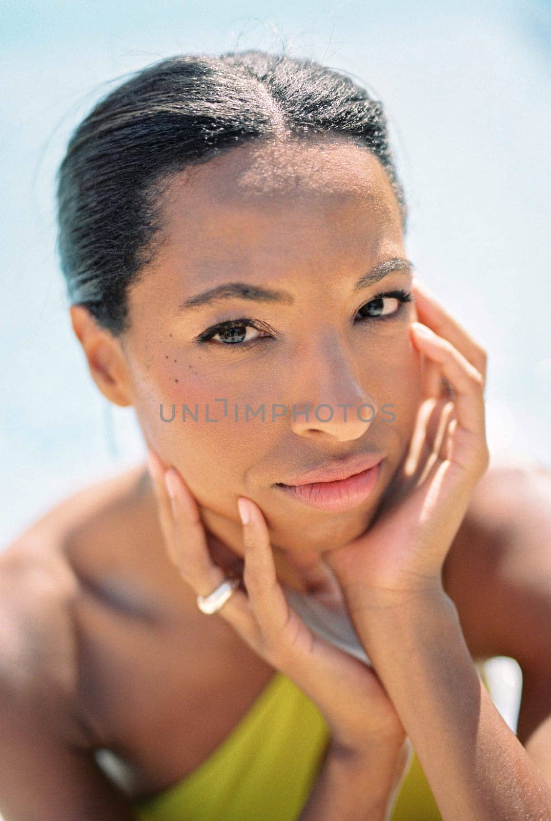 Young woman in a swimsuit sits in the sun resting her chin on her hands by Nadtochiy