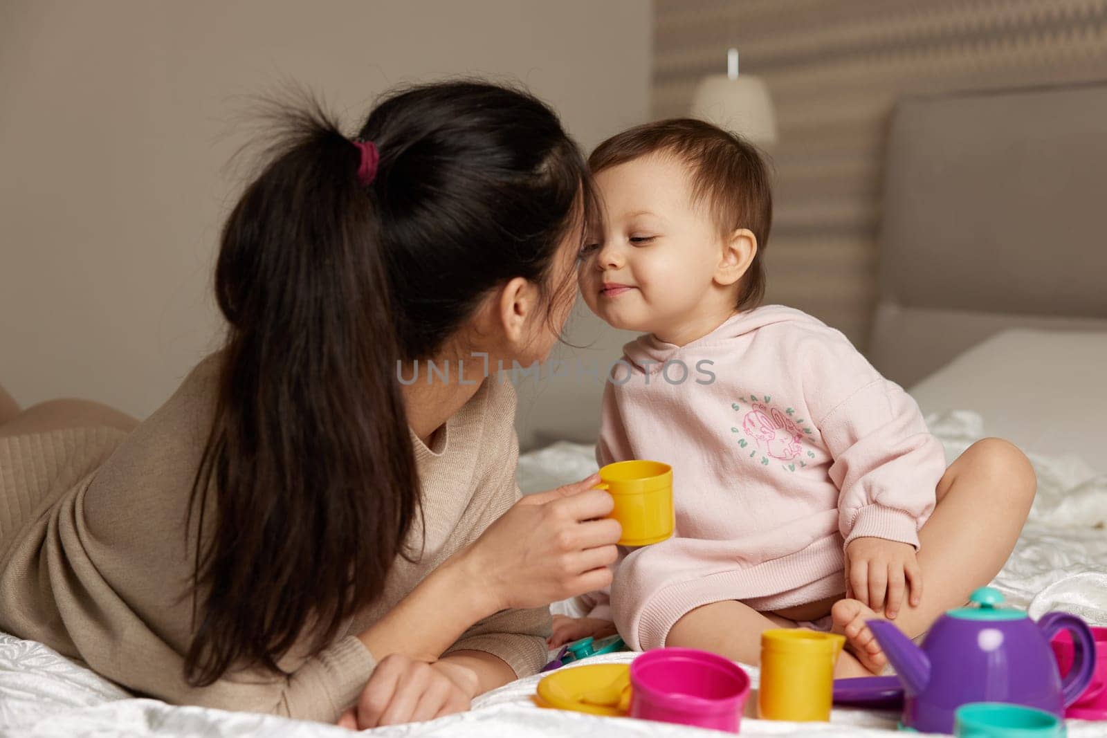 mother and little child daughter playing tea party and spending time together in bedroom, family having fun