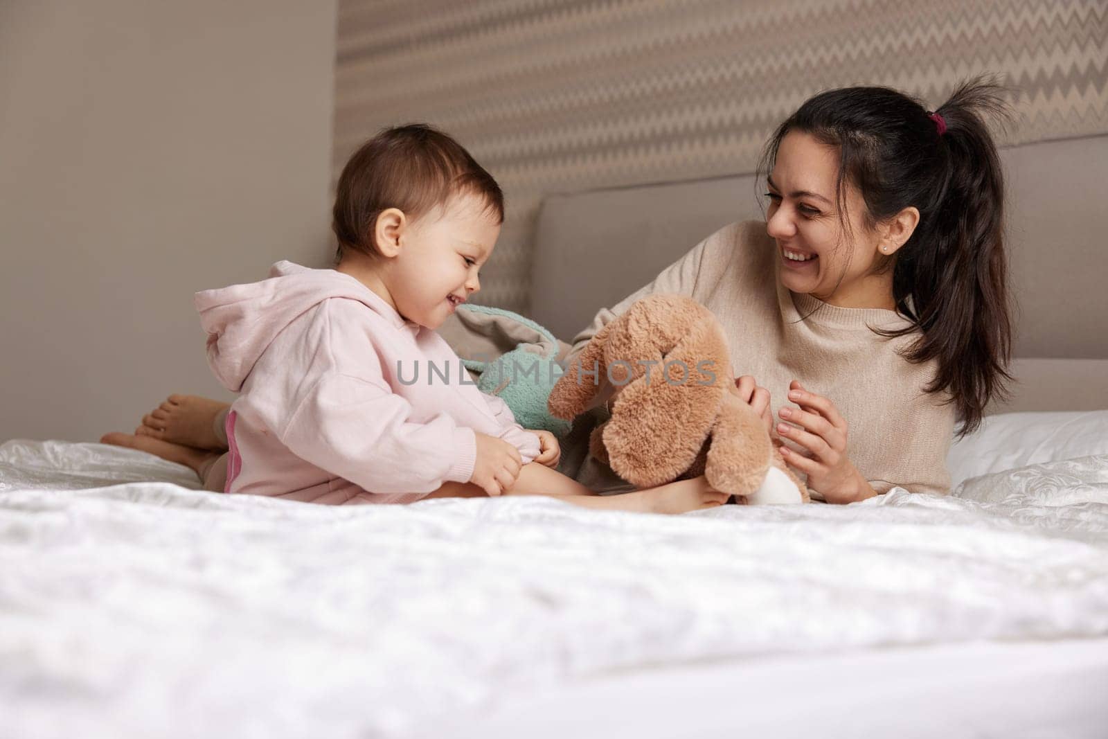 happy mother and her little child daughter playing with bunny toys in bedroom, family having fun