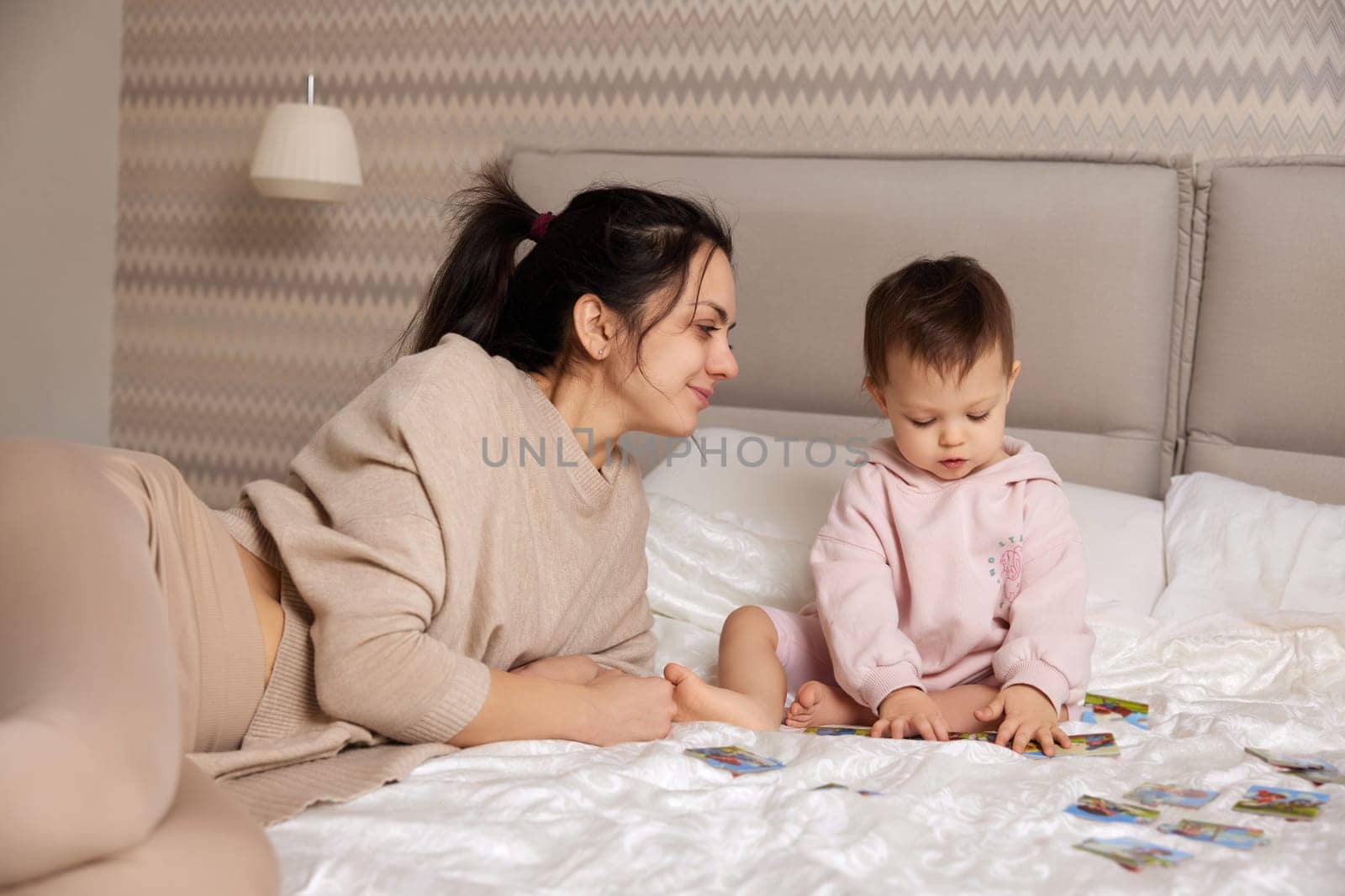 cheerful mother playing puzzle together with her little child girl in bedroom