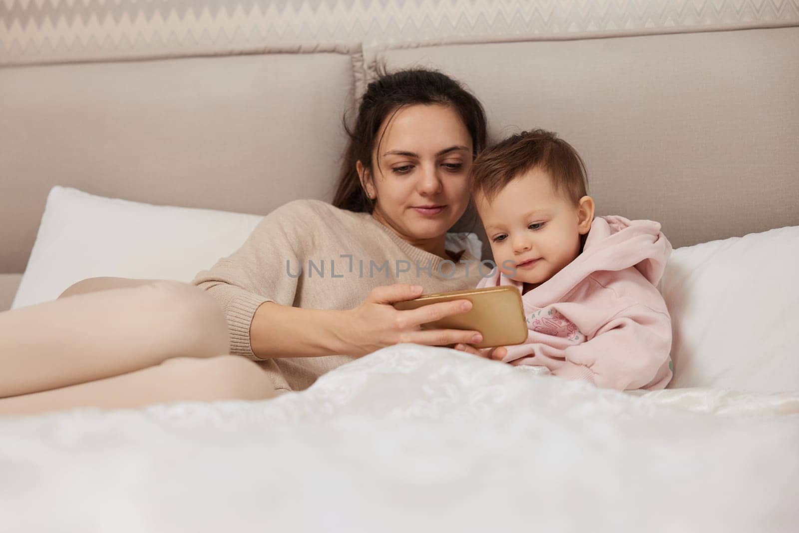 Caucasian mother and child playing online game on smartphone in bedroom at home