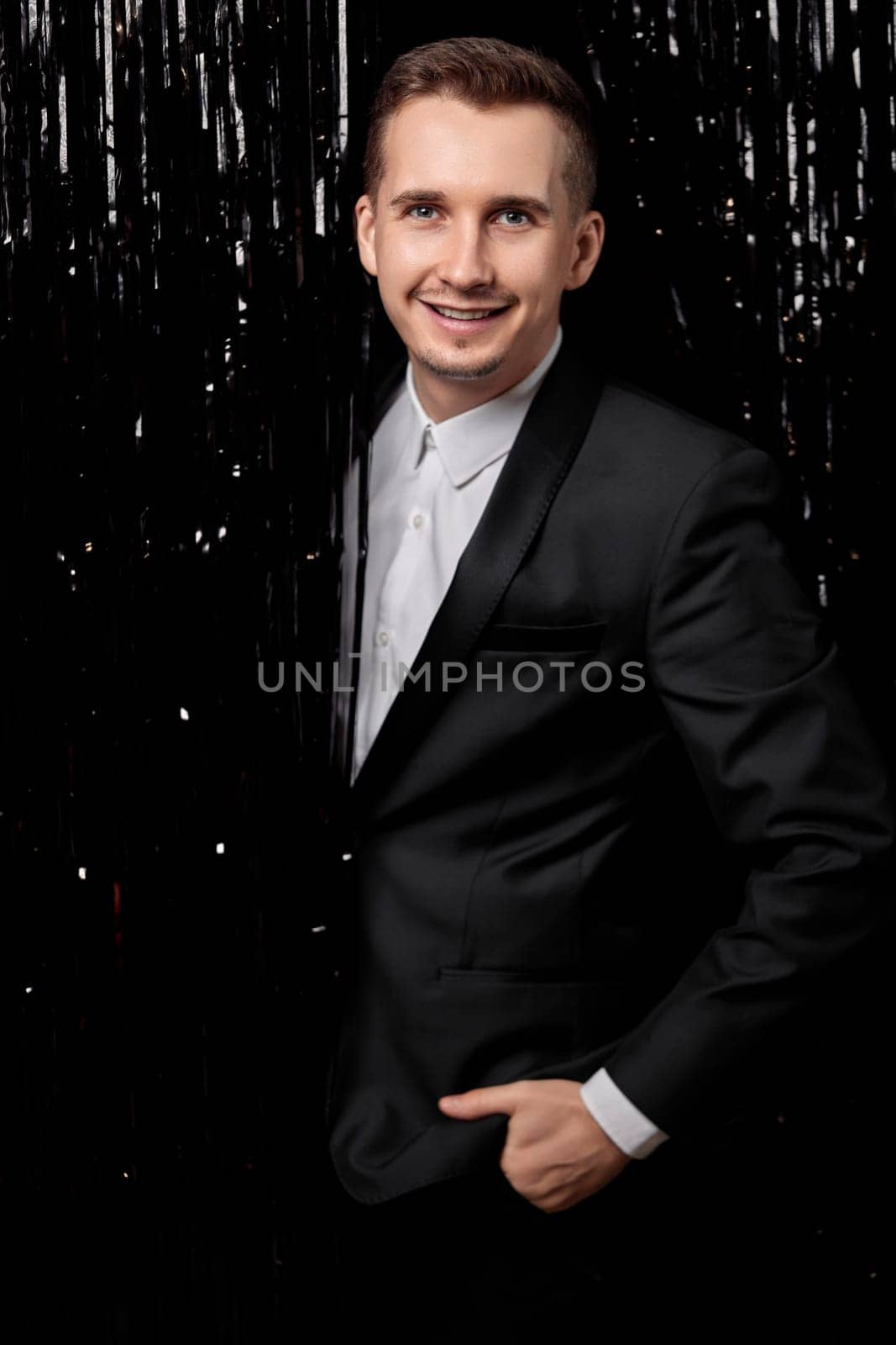 Happy handsome man in black jacket smiling on glitter background.