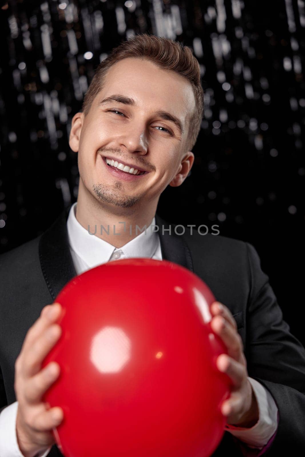 caucasian man in black jacket with red air balloon on dark glitter background. new year party