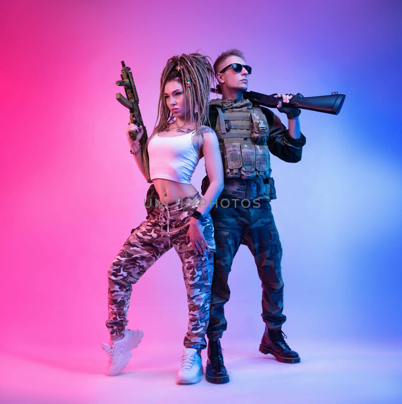 daring stylish girl with an automatic rifle and a guy in military clothes with an airsoft gun in neon light on a bright neon background pose fashionably by Rotozey
