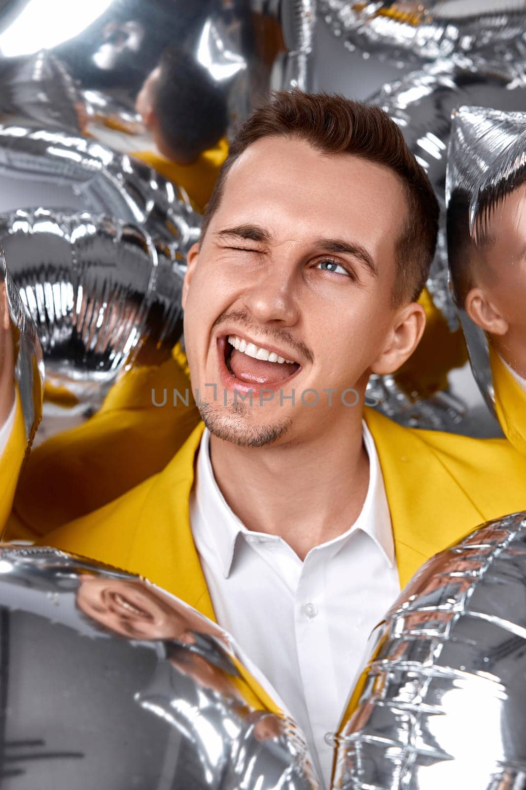 happy winking man in yellow jacket with a lot of silver air balloons. birthday party