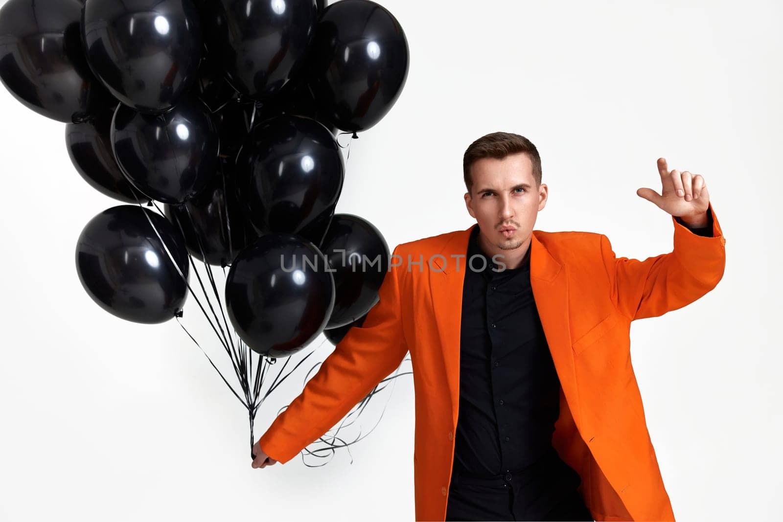 handsome man in orange jacket with black air balloons on white background. birthday party