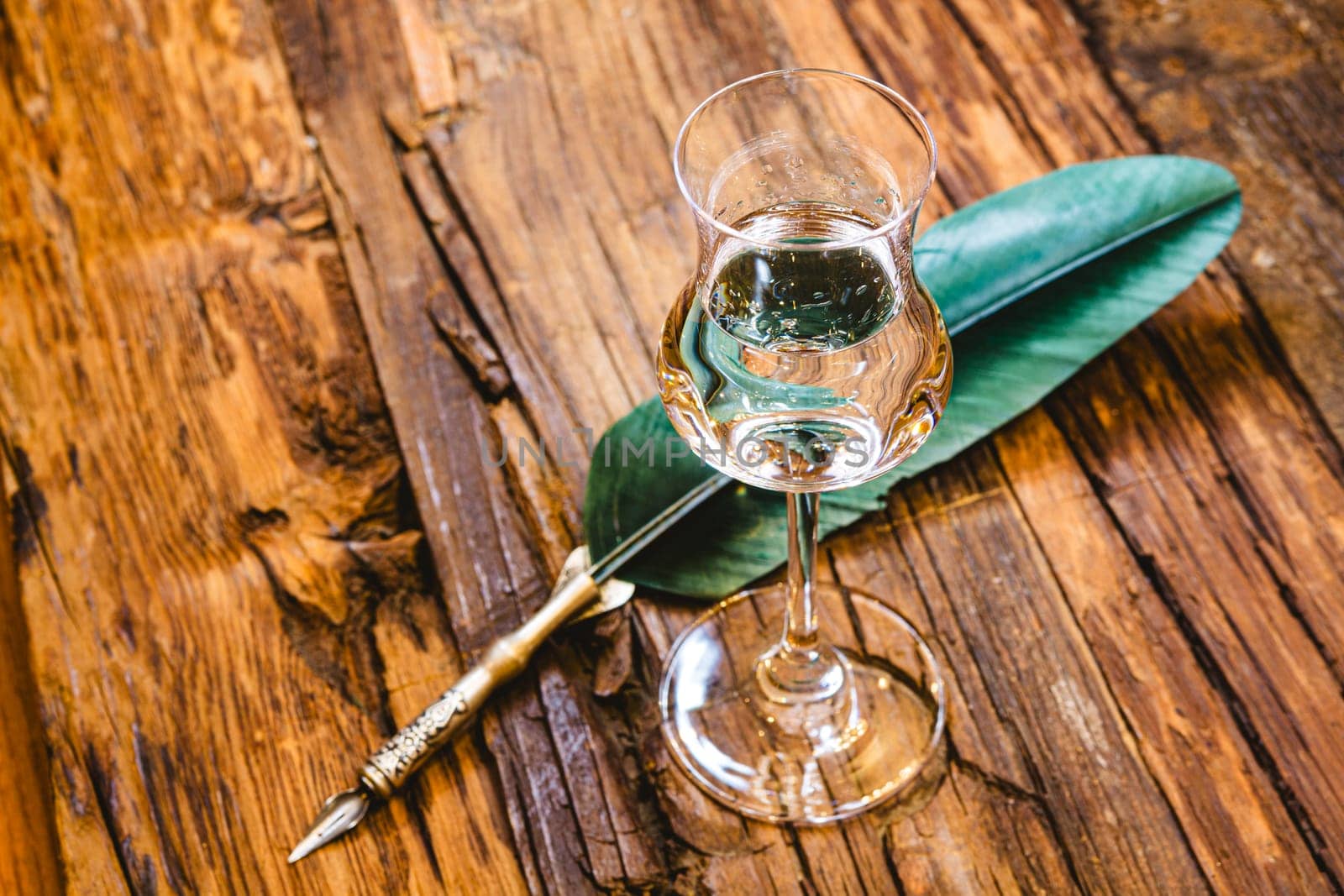 Small shot glass on the old bar counter. Vintage wooden background in pub or bar, night mood. Place for text, toning.