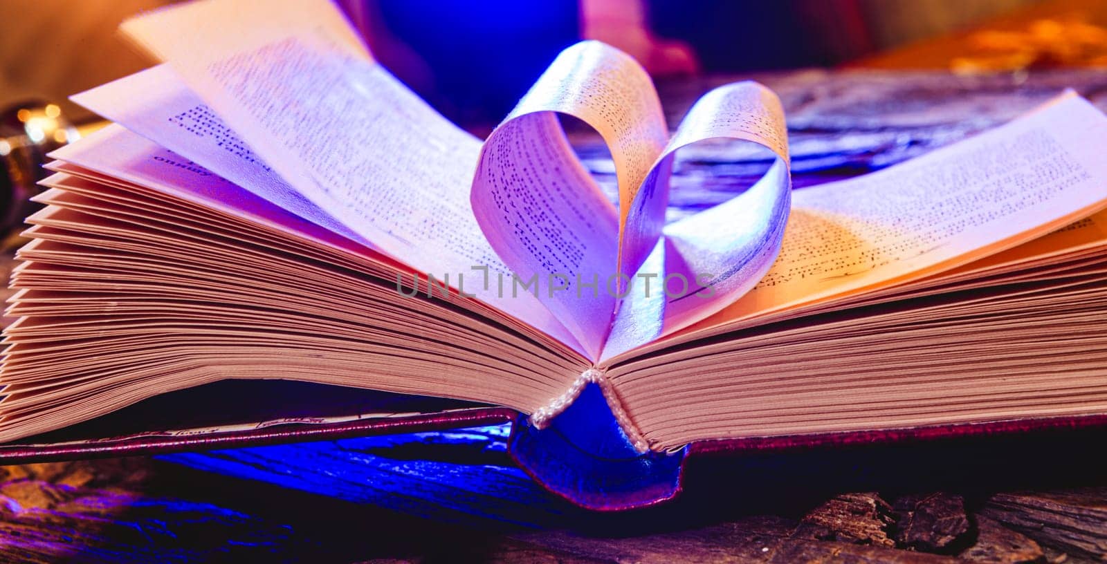 Stack of books in the colored cover lay on the table. Open book with curled leaves in the shape of a heart. Library, education. Love of books, reading. Empty space for Your text on the left. Shallow dof
