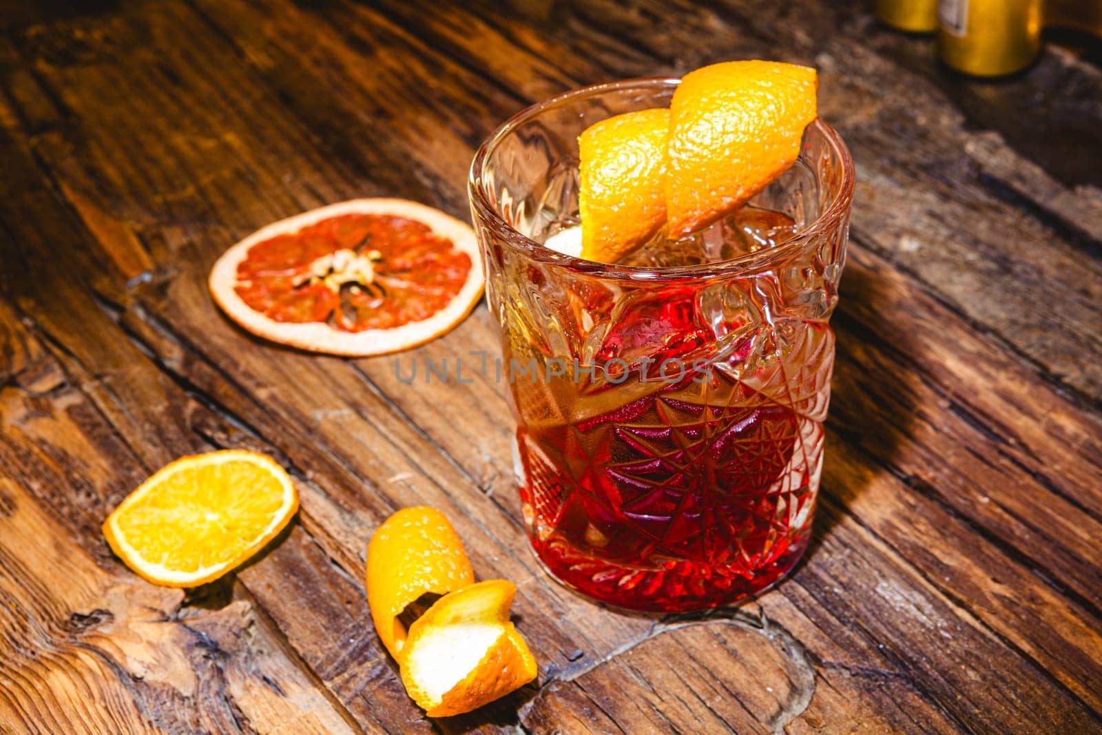 Delicious old fashion cocktail in the etched glass with ice and orange slices, dark wooden background. Shallow dof.