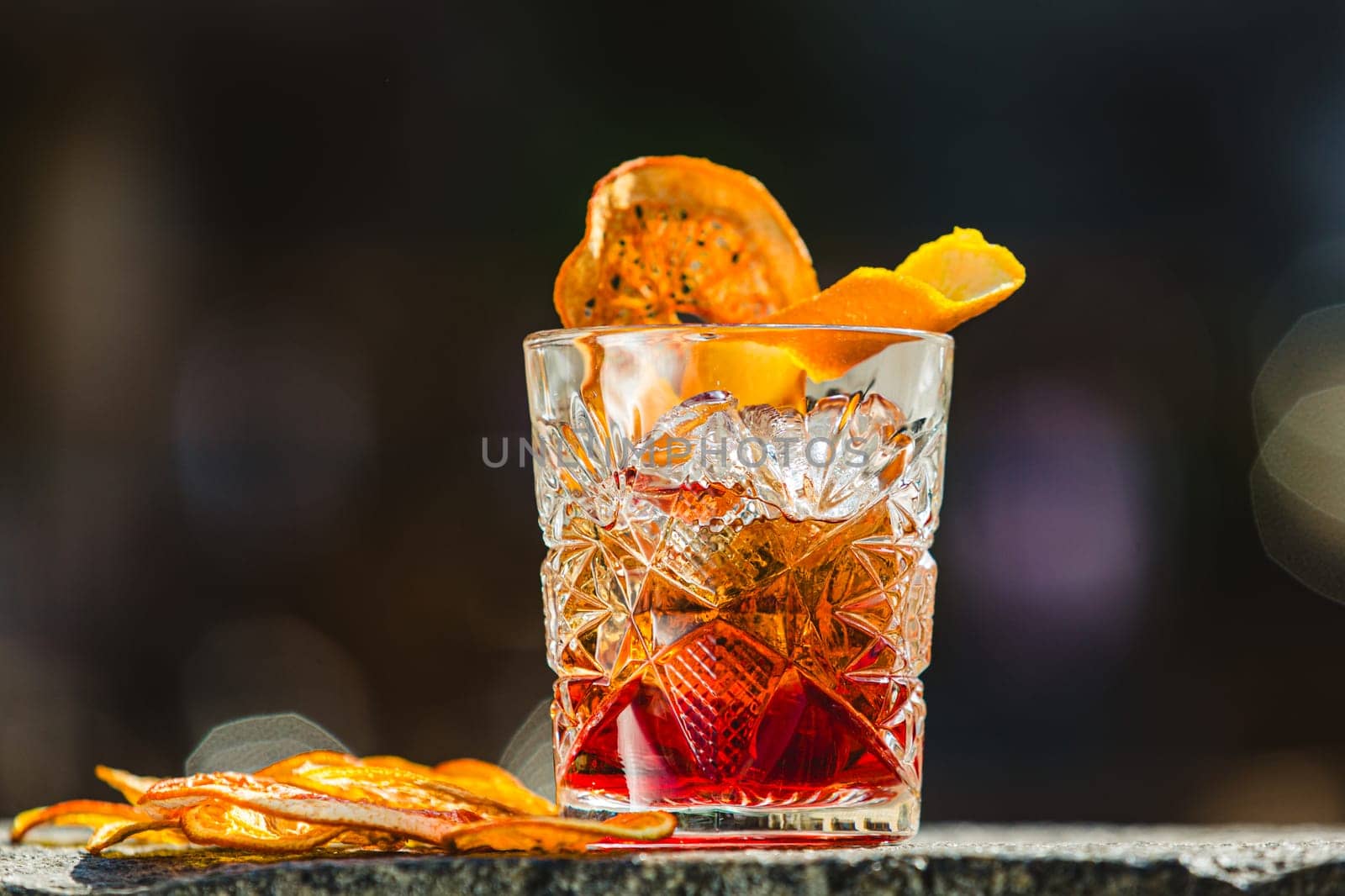 Delicious old fashion cocktail in the etched glass with ice and orange slices, dark wooden background. Shallow dof