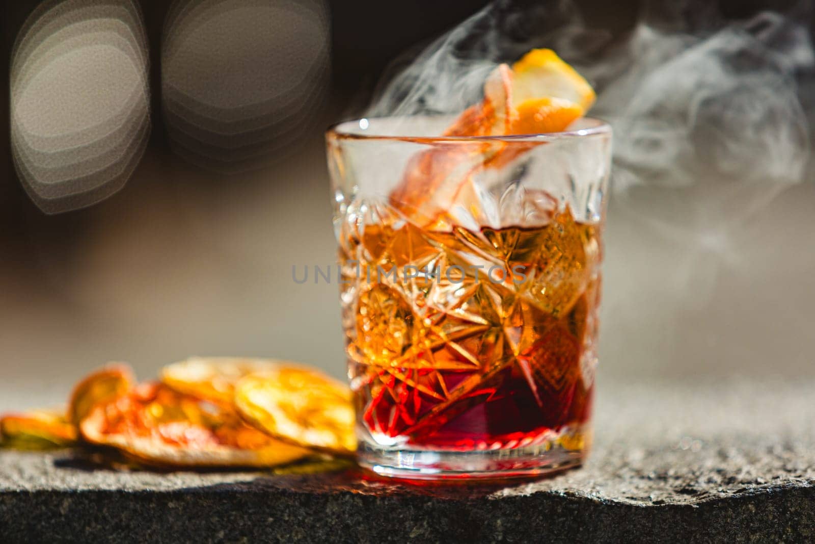 Delicious old fashion cocktail in the etched glass with ice and orange slices, dark wooden background. Shallow dof