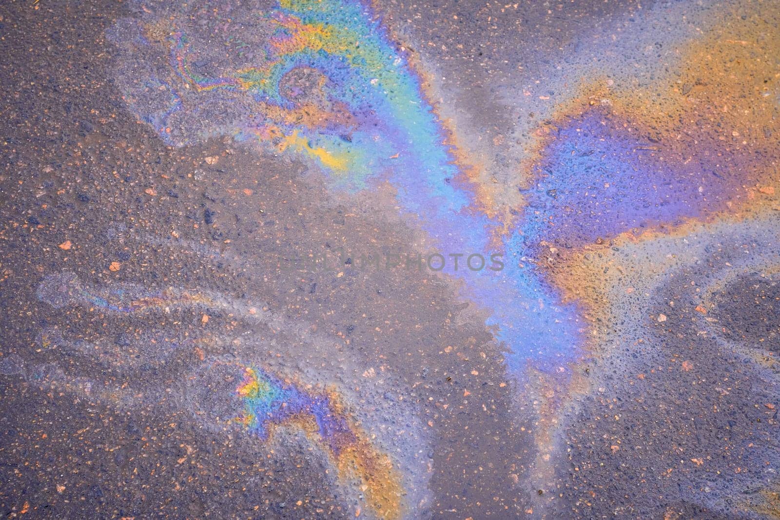 Texture of colorful petrol oil spill on wet pavement. Slick industry oil fuel spilling water pollution.