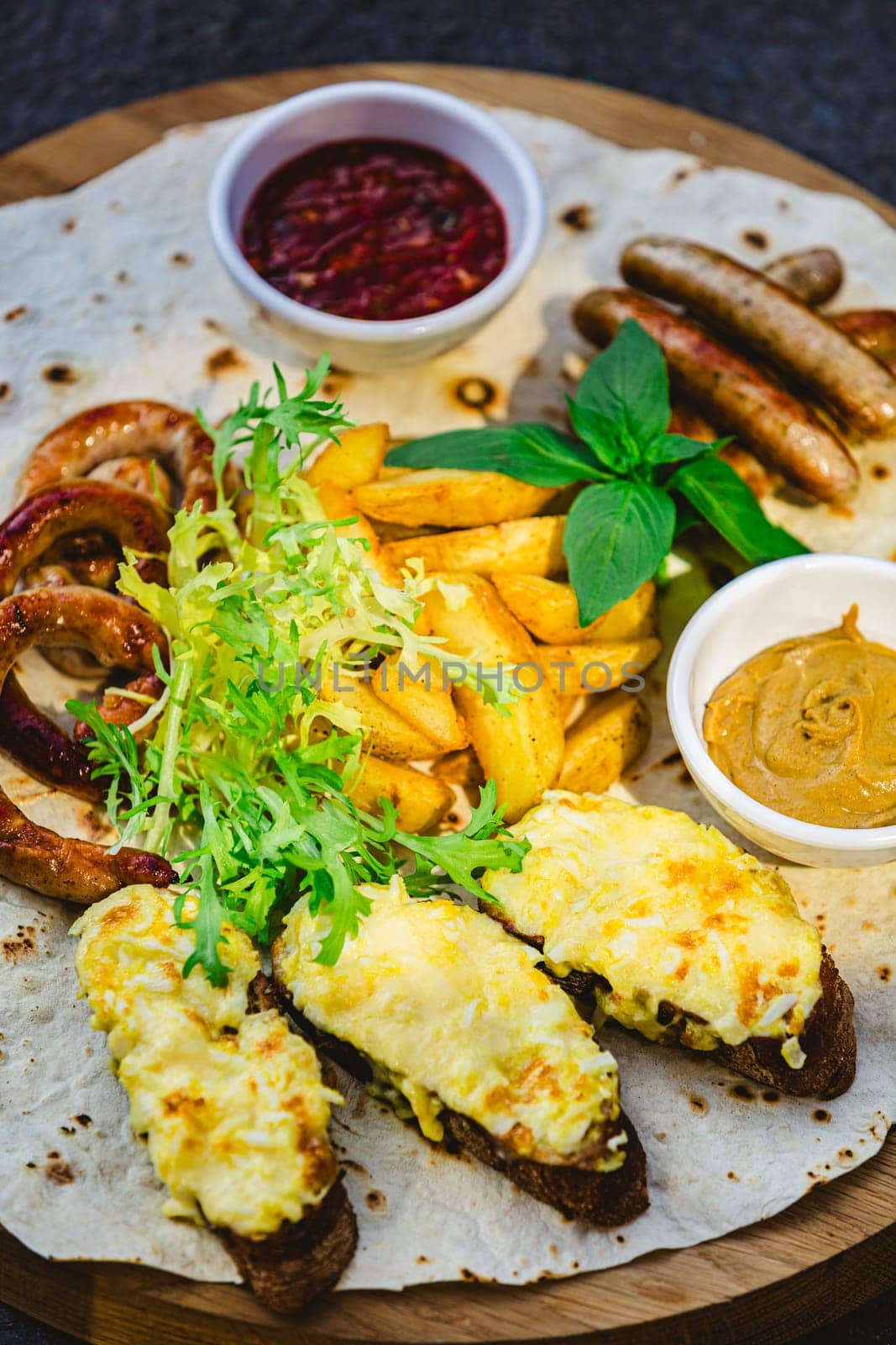 German style grilled sausages with potato wedges and bread with cheese and sauces close-up on a wooden tray on the table. Shallow dof