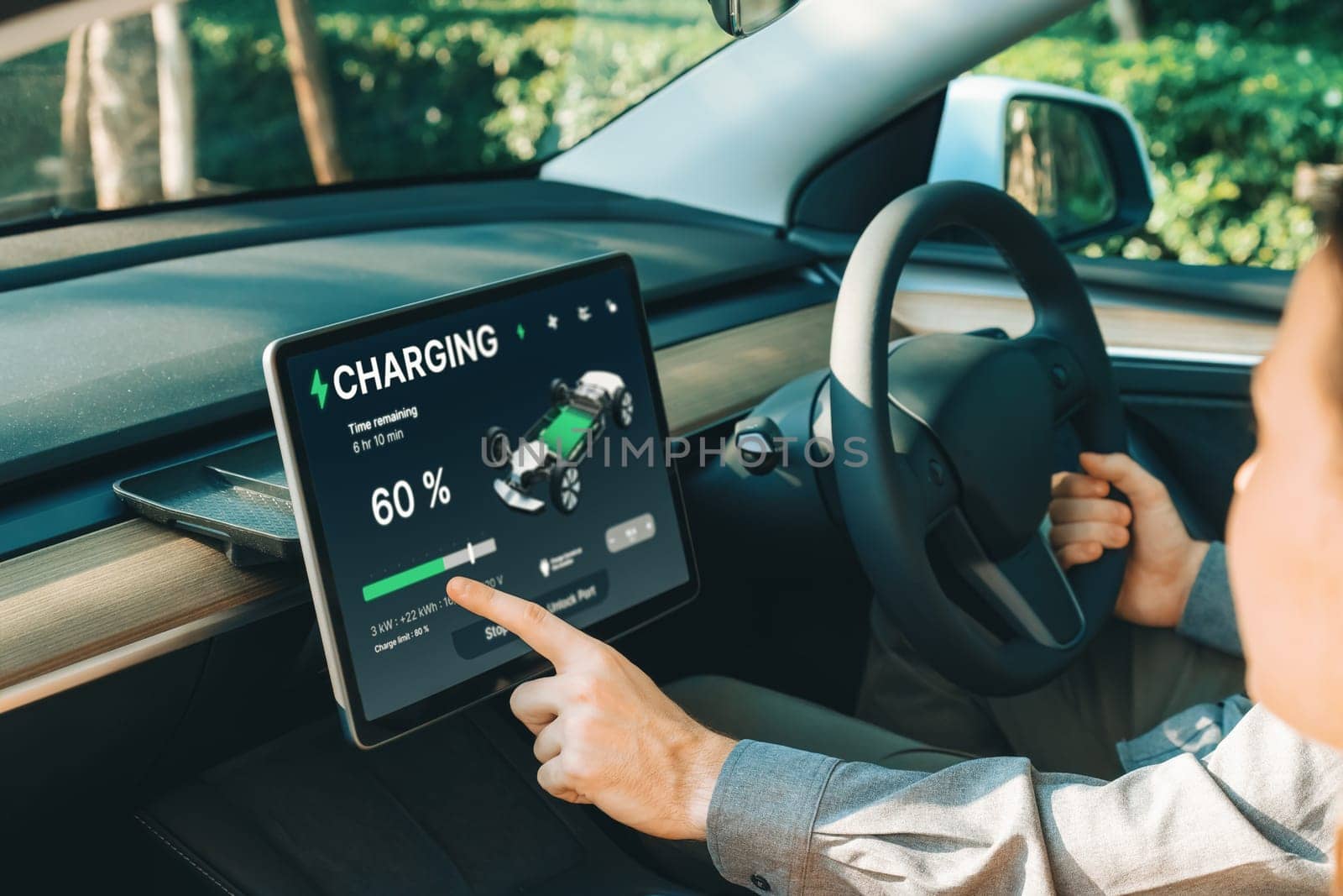 Electric car driver checks battery charging status app screen in car innards by biancoblue