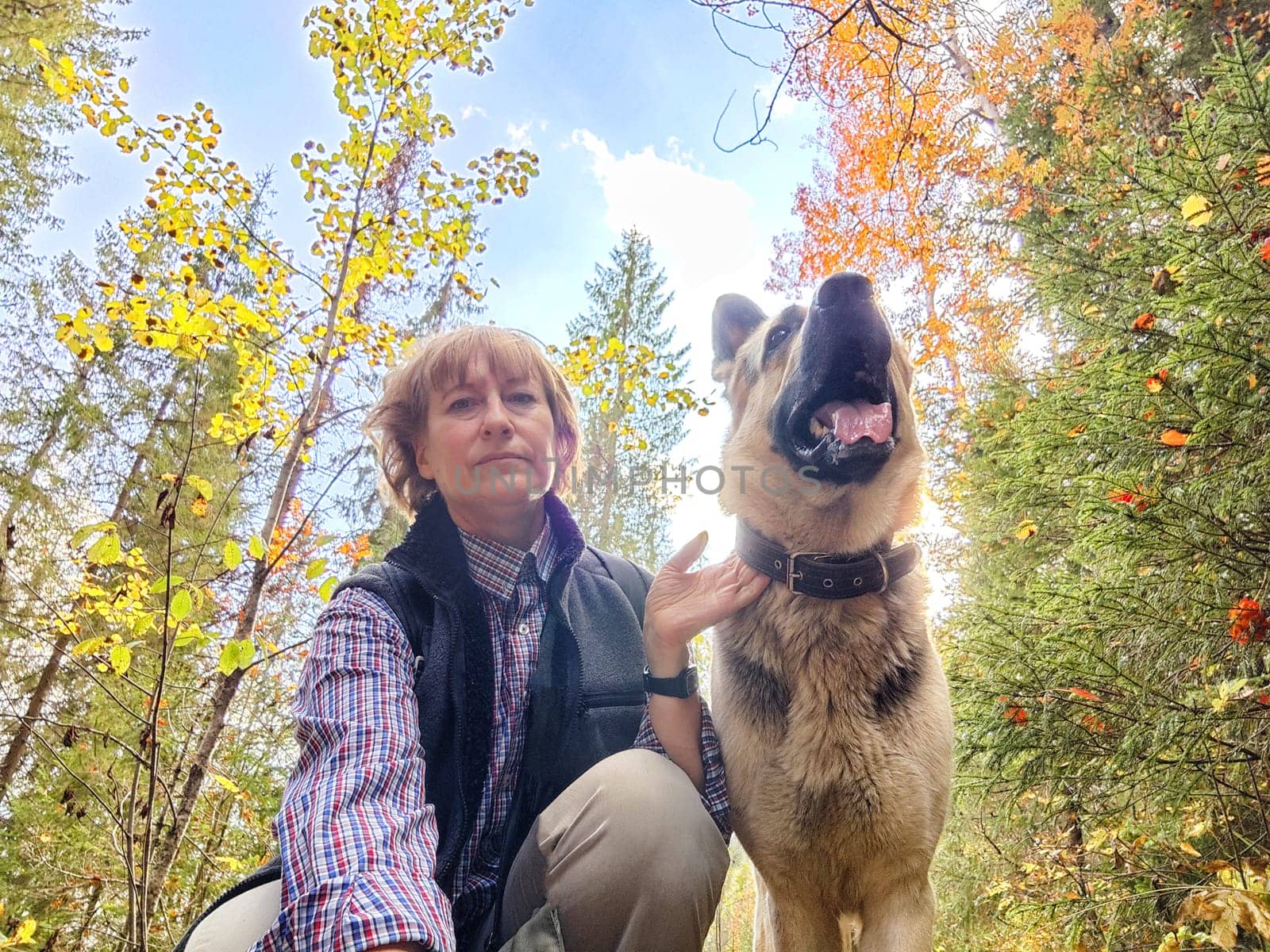 Adult girl with shepherd dog taking selfies in forest. Middle aged woman and big shepherd dog on nature. Friendship, love, communication, fun, hugs