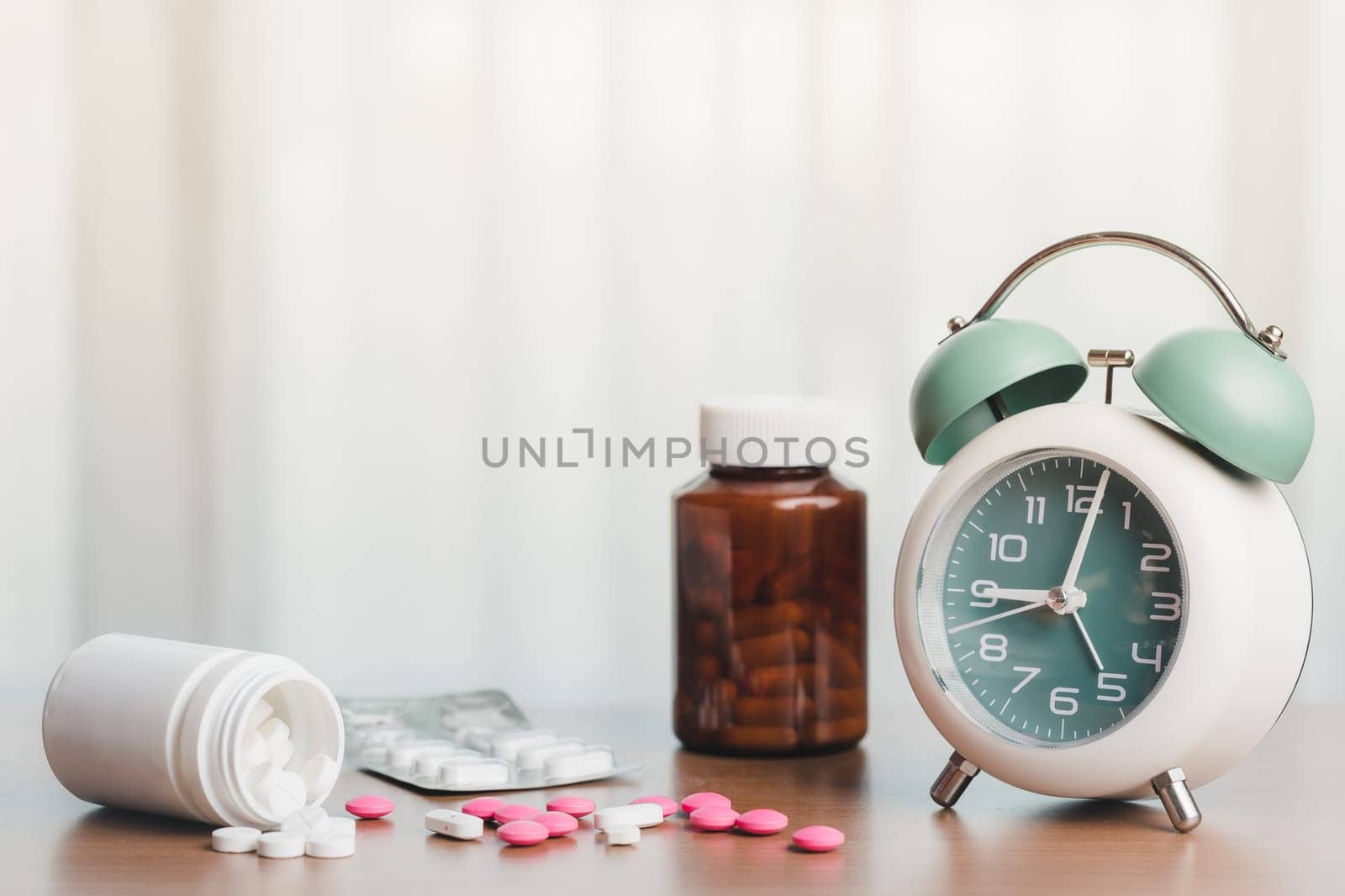Healthcare essentials with an alarm clock, pills, and medicine bottle on a white curtain background by iamnoonmai