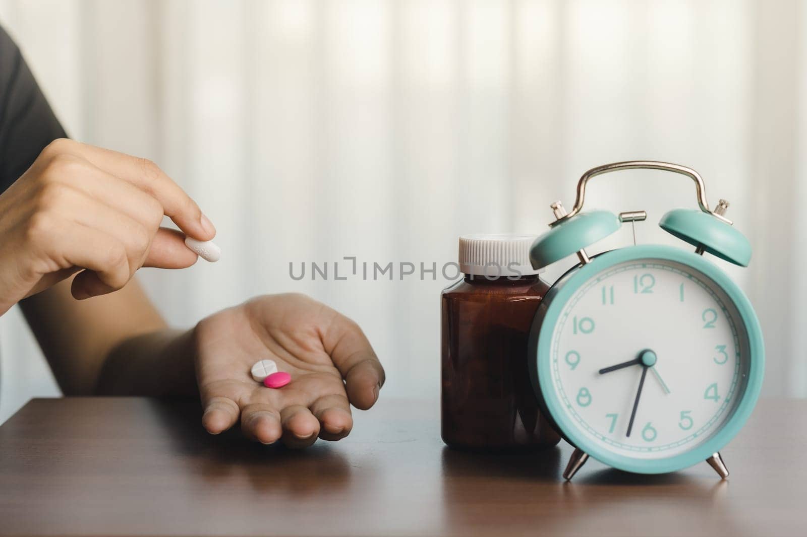 Person holding a pill with a medicine bottle and an alarm clock for time management, deadlines, and the concept of medical and health care 