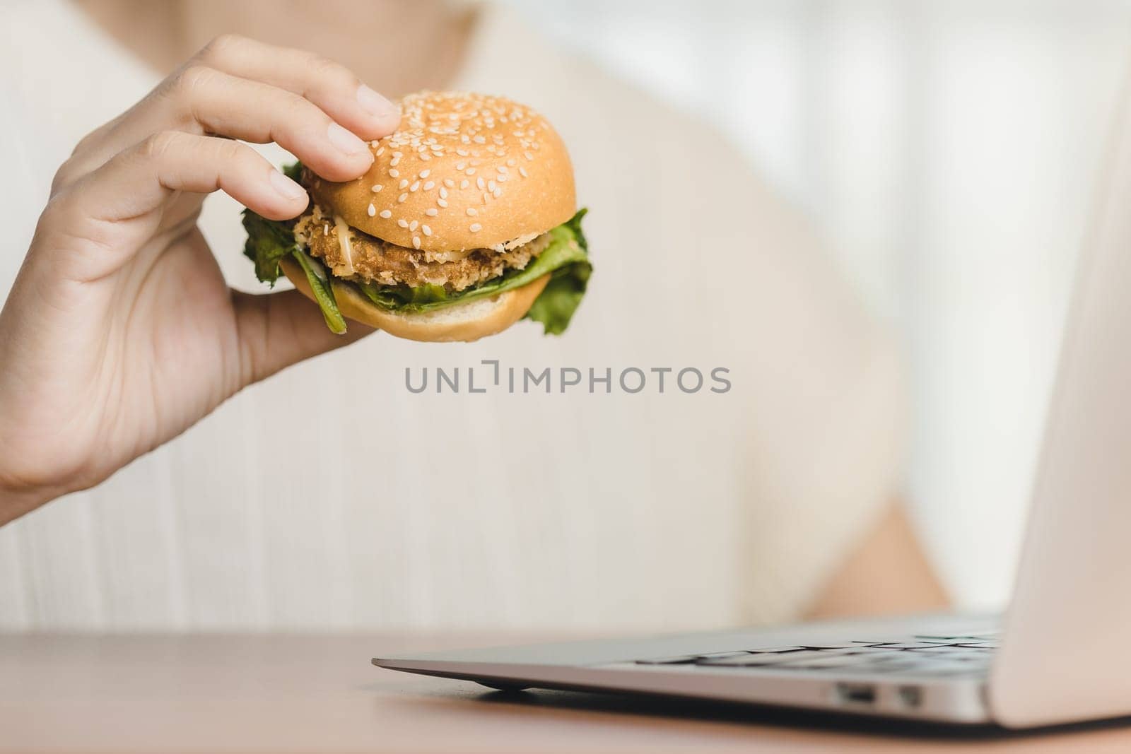 Person enjoying a delicious hamburger meal with cheese, lettuce, tomato, and beef, held in their hands during working for eating fast food at work concept