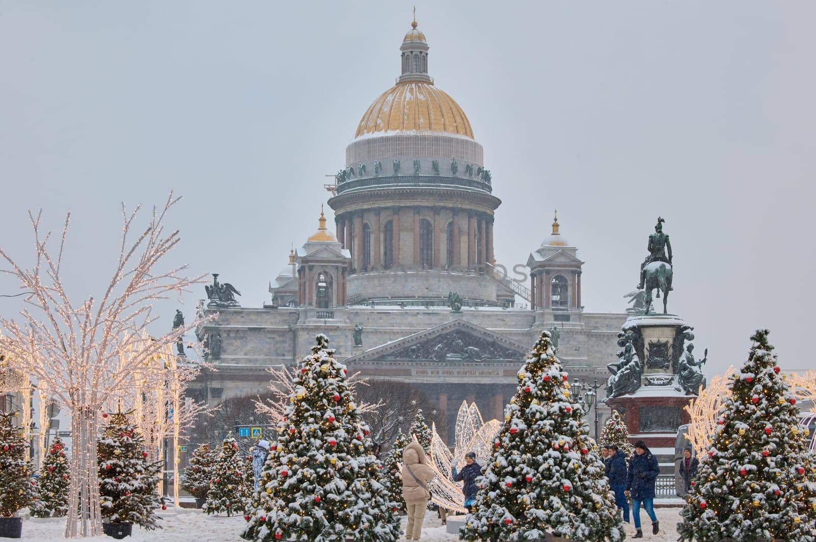 Russia, St Petersburg, 30 December 2023: people walk among Christmas trees in heavy snowfall, a park organized on holidays near St. Isaac's Cathedral and the monument to Emperor Nicholas II. High quality photo