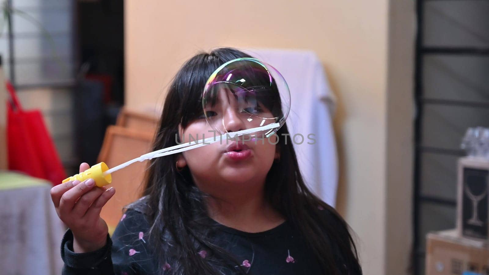 A cute little girl blowing smoke soap bubbles inside her house.