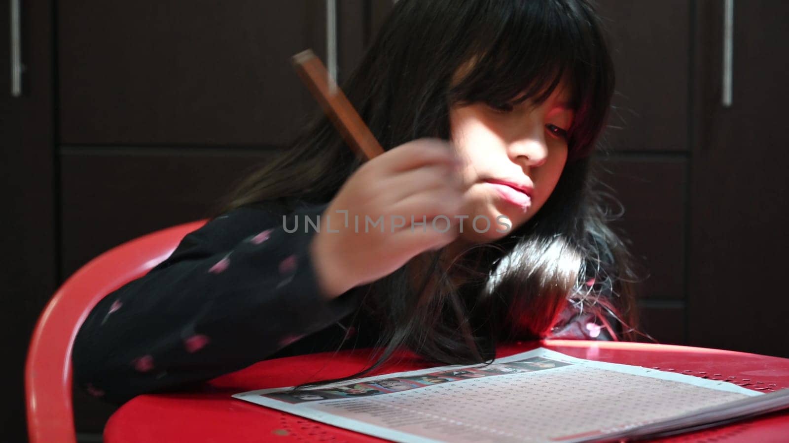 Girl with pencil looking for words in the newspaper crossword. by Peruphotoart