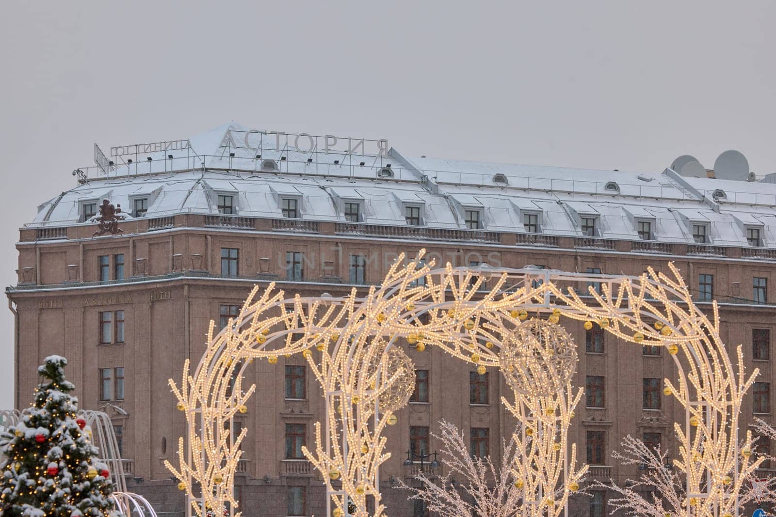 Russia, St Petersburg, 30 December 2023: Hotel Astoria through Christmas trees in heavy snowfall, a park organized on holidays near St. Isaac's Cathedral. High quality photo