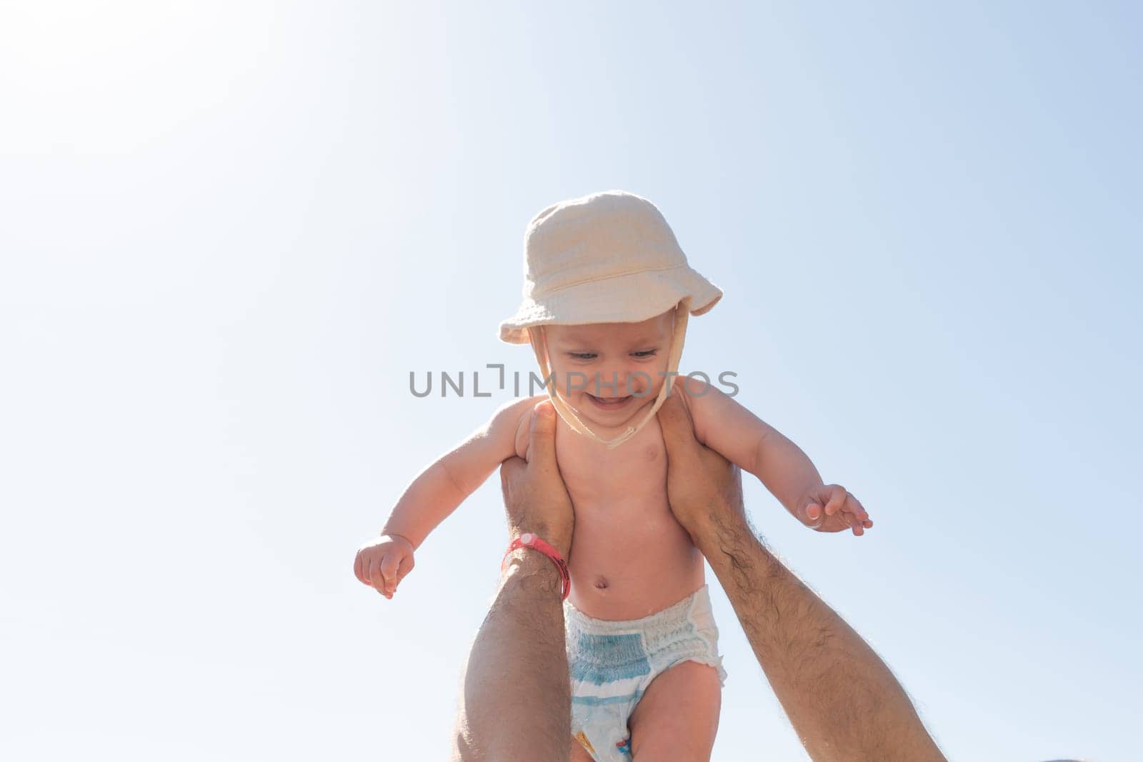 Celebrating a special moment, a father lifts his baby high under a radiant sun, symbolizing nurturing and joy. Concept of early development and playful parenting