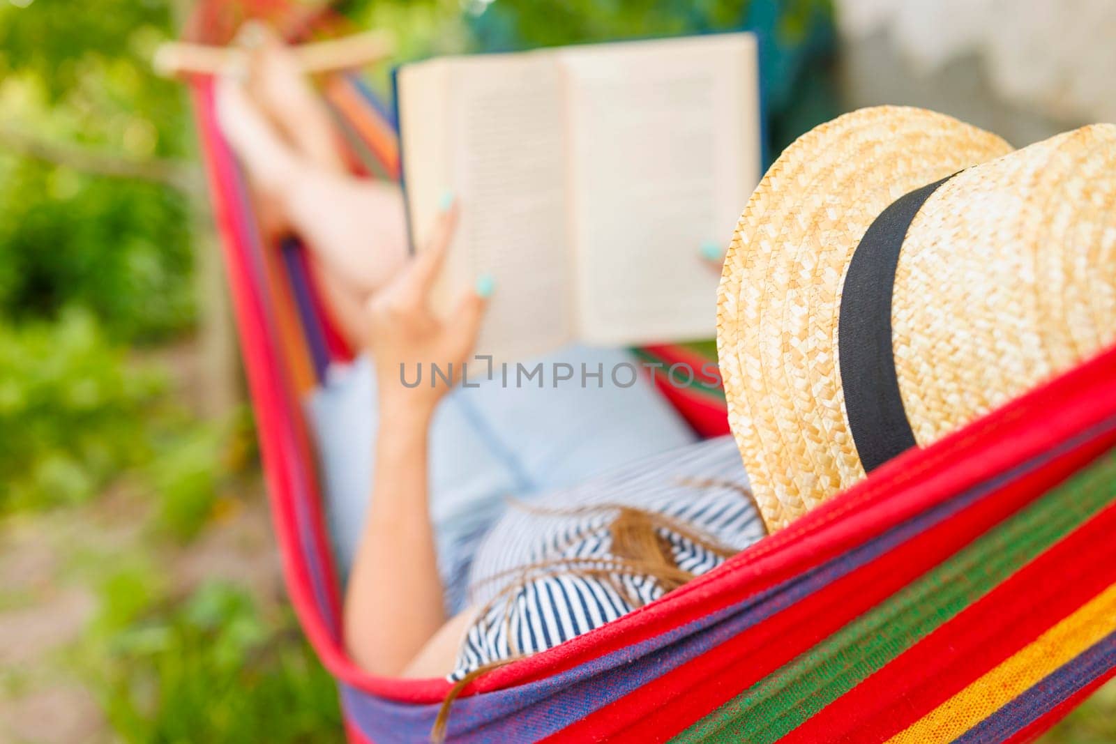 Woman enjoying a book in a hammock on a sunny day, with straw hat and garden background.