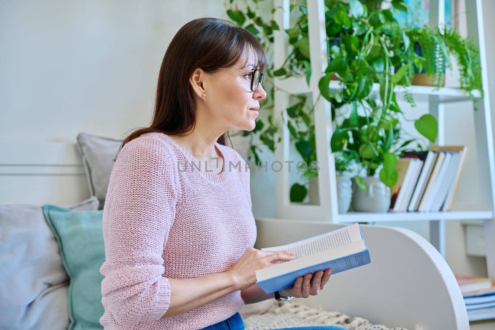 Mature woman reading paper book sitting on couch at home. Relaxation, literature hobby, fiction, lifestyle, people concept