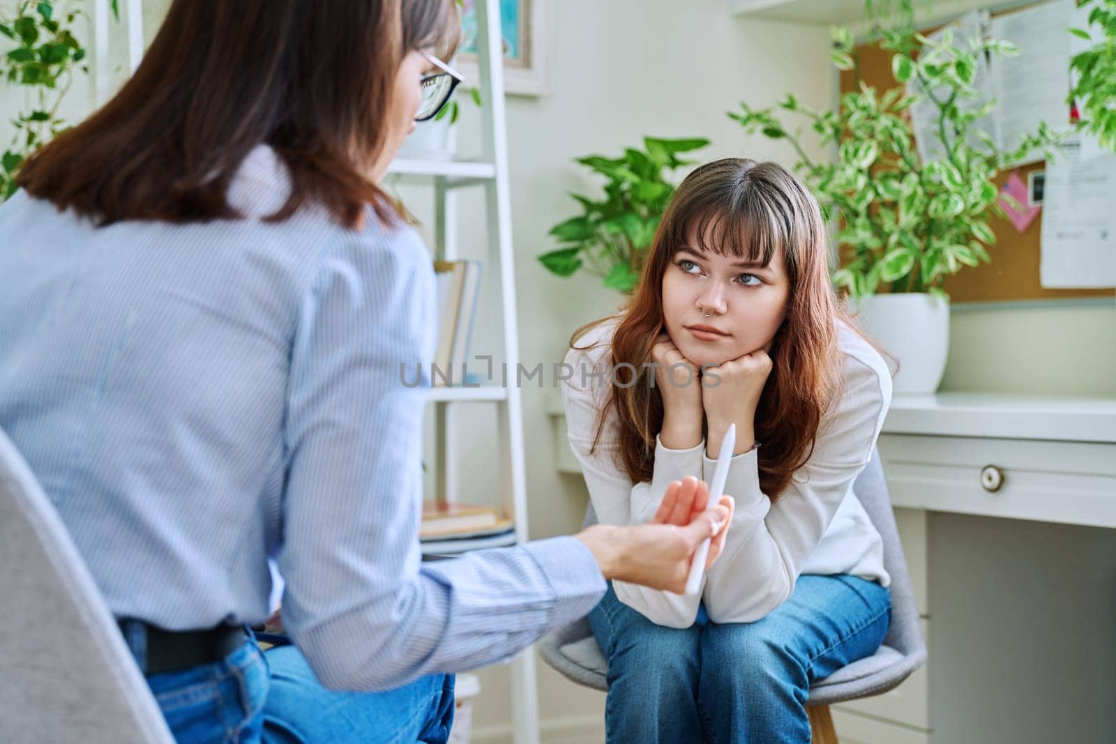 Sad, serious teenage girl at session in office of mental professional by VH-studio