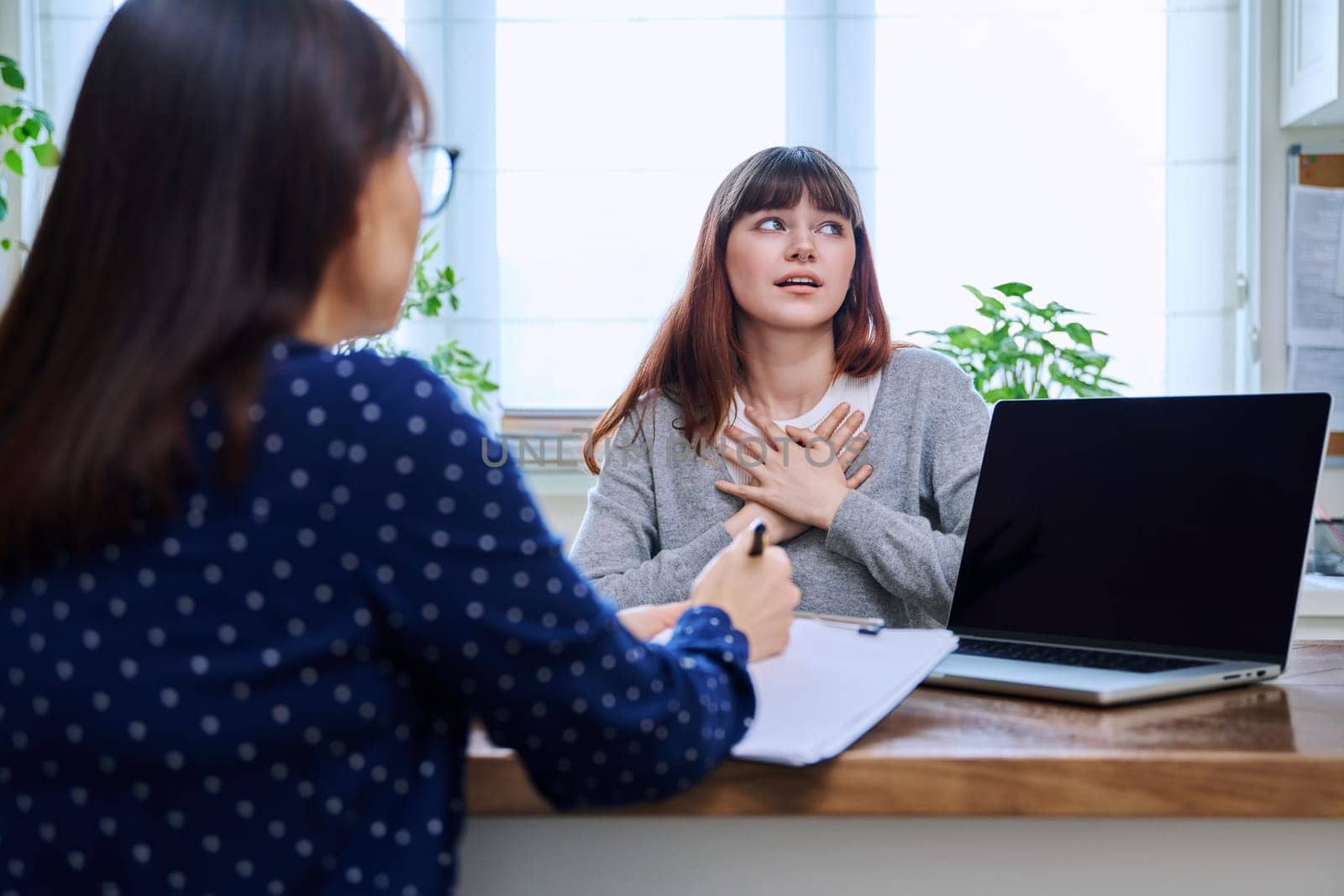 Sad, serious teenage girl at a session in the office of a mental professional, psychologist, counselor, social worker. Feelings, difficulties, problems, depression, stress, youth concept