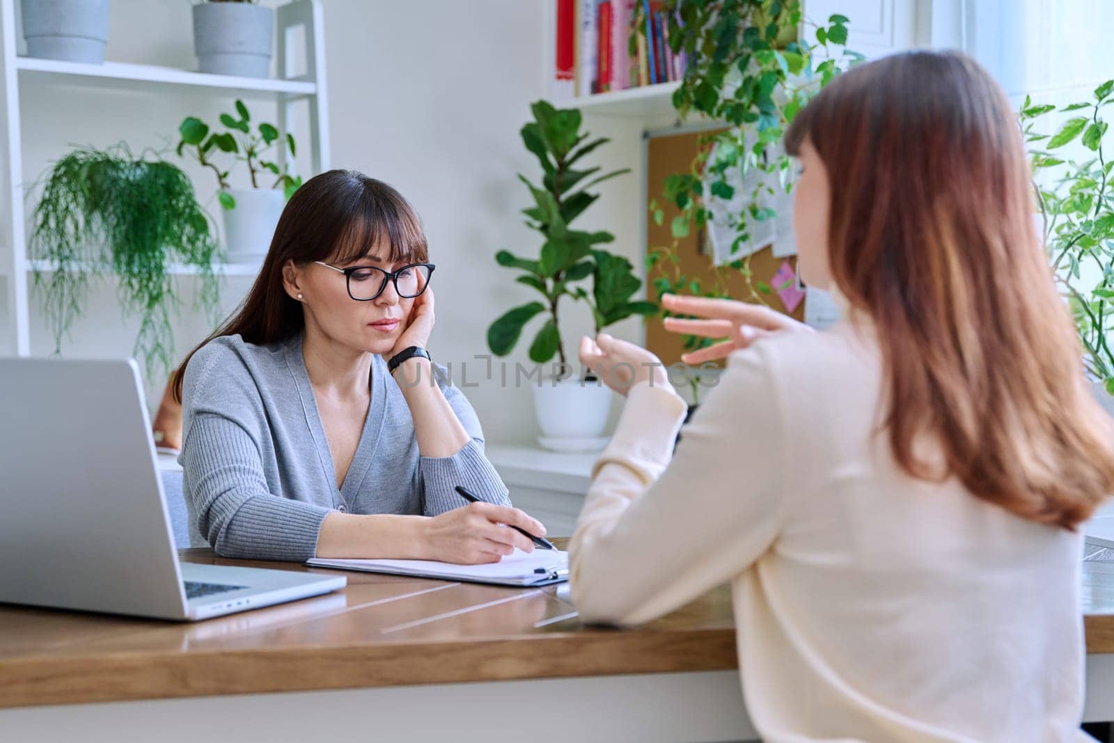 Middle-aged female psychologist, psychotherapist, counselor, social worker working with young woman patient. Psychology therapy professional help consultation treatment support mental health concept