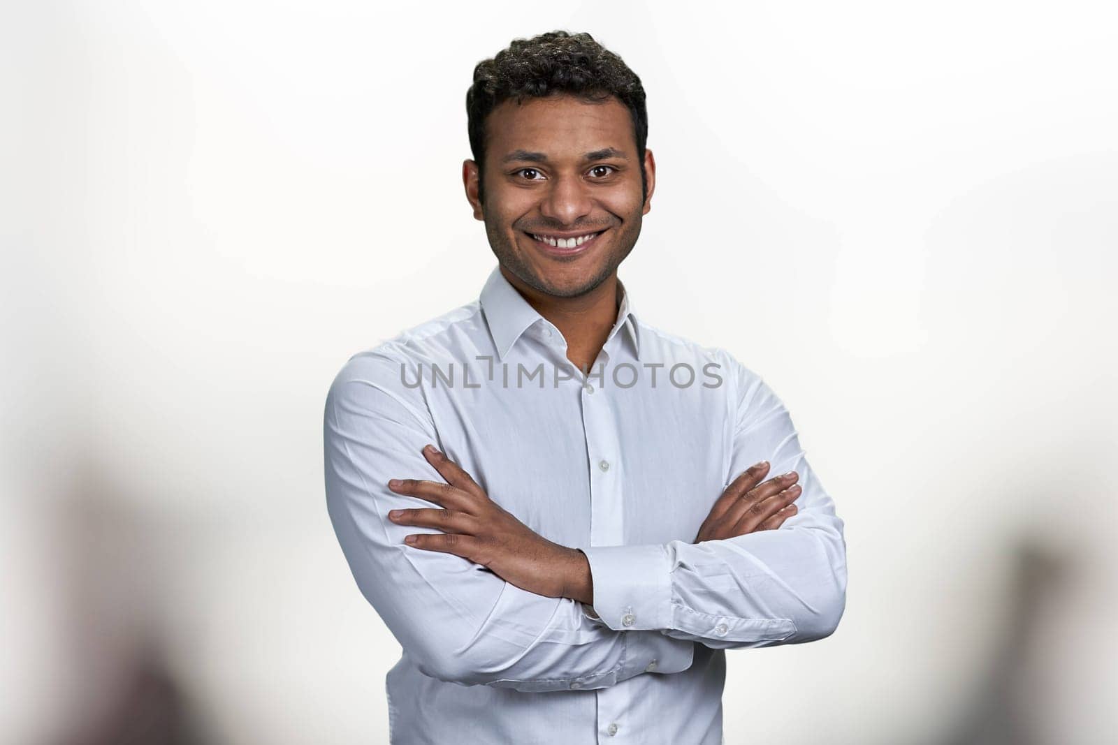 Handsome smiling man with crossed arms looking at camera. Portrait of indian businessman on blurred background.