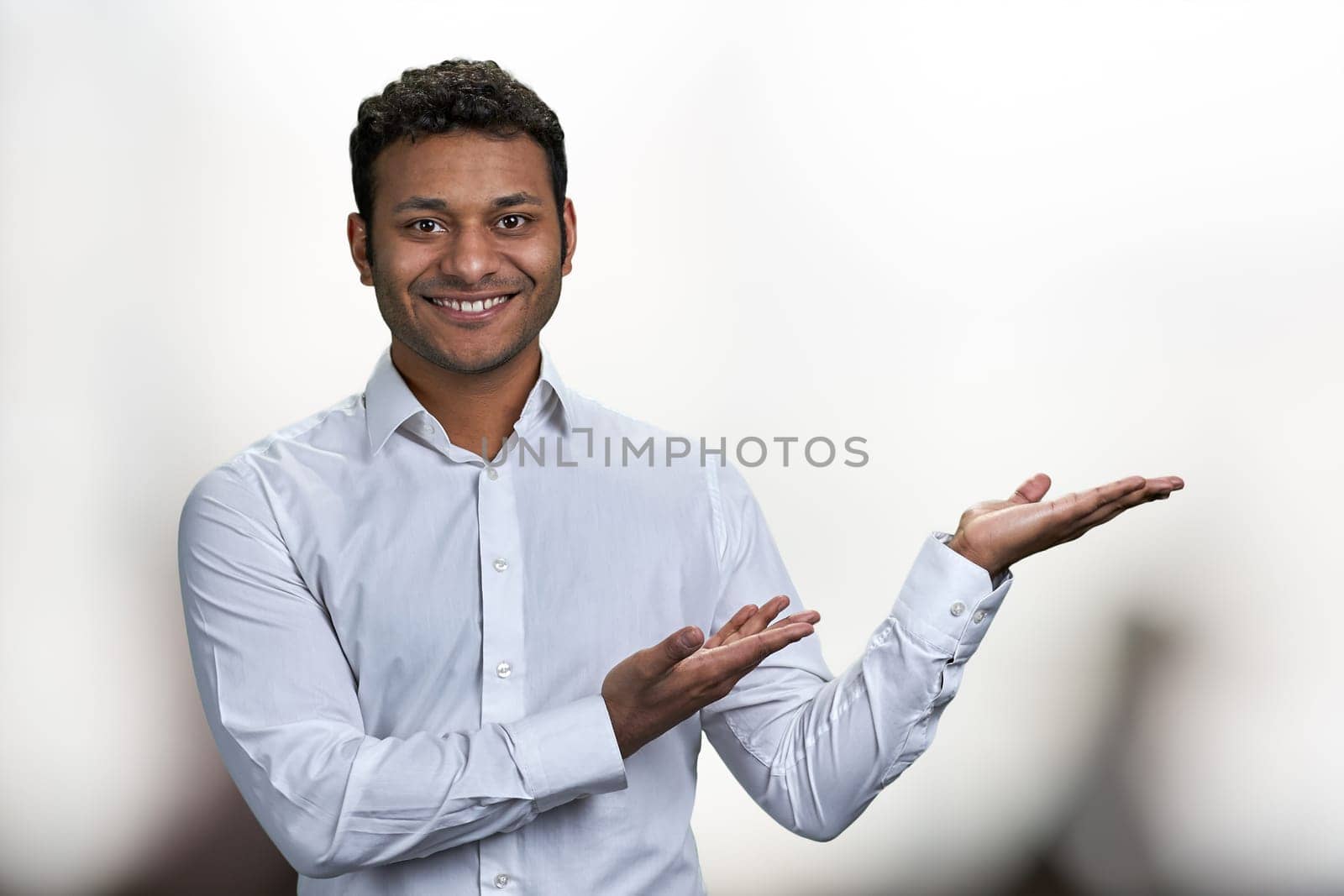 Young handsome man pointing to the side with hand and open palm presenting something. Place for advertisement.