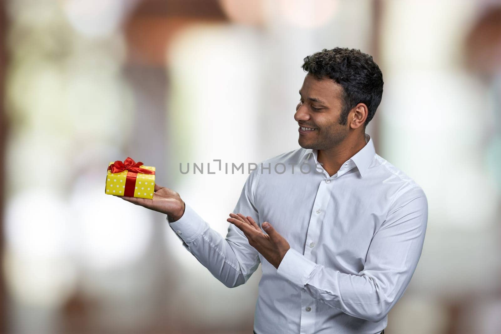 Cheerful handsome man presenting gift box on blurred background. Christmas sales concept.