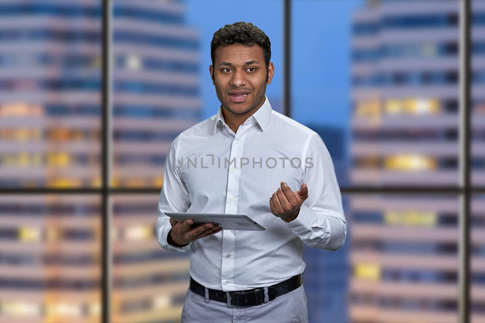 Young Indian business man giving a presentation using digital tablet. City night background inside office.