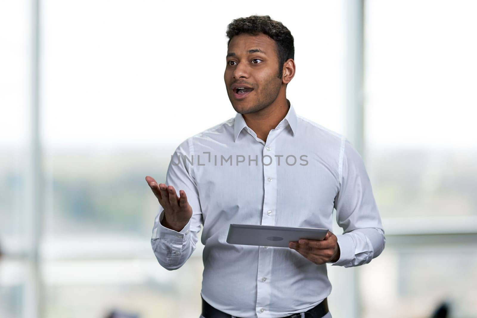 Attractive young businessman giving presentation. Blur interior background. Business coach using tablet device.