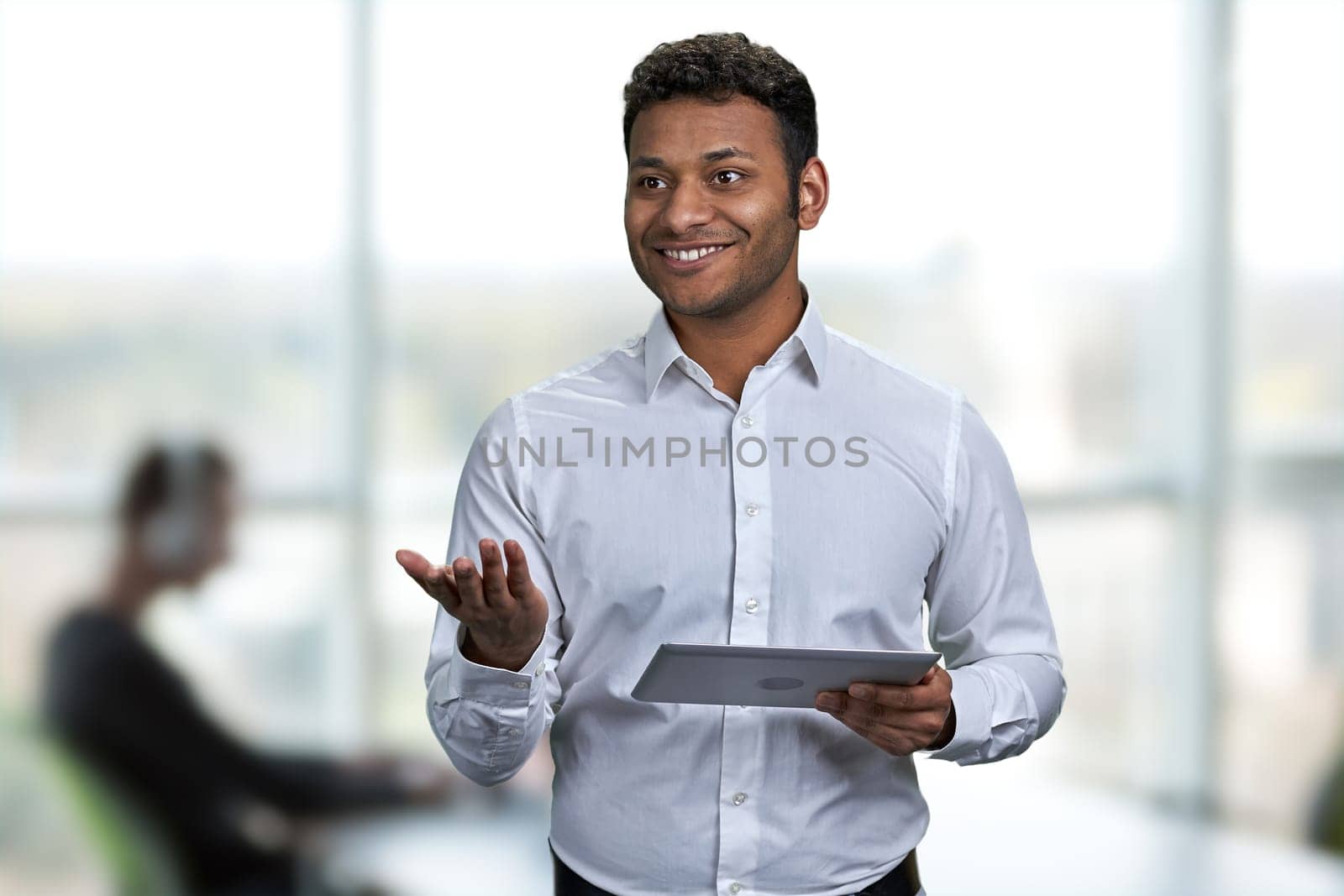 Cheerful businessman wearing white shirt holding digital tablet pc. Blur office interior background.