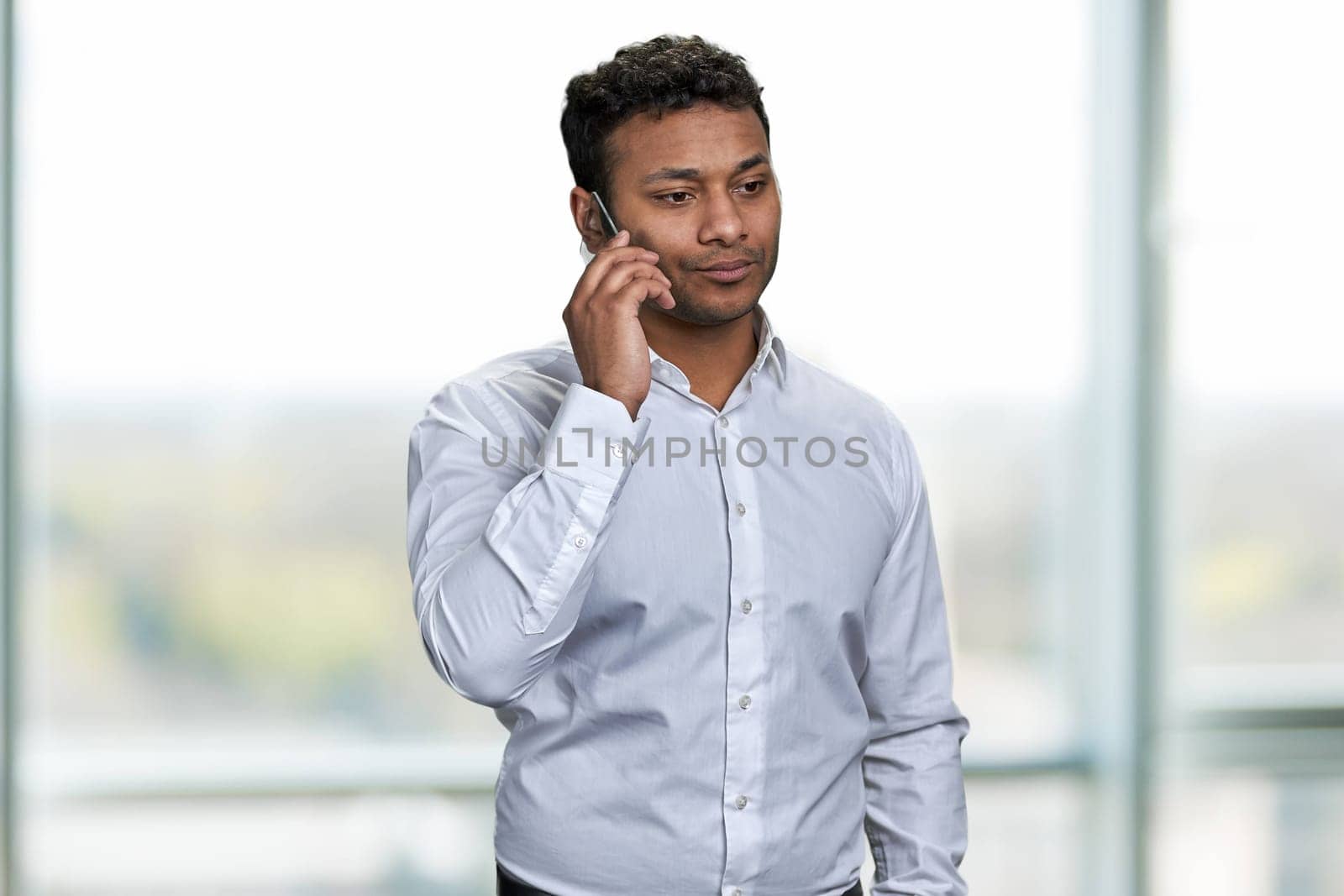 Confident young businessman wearing white shirt talking on transparent phone phone. by super_picture