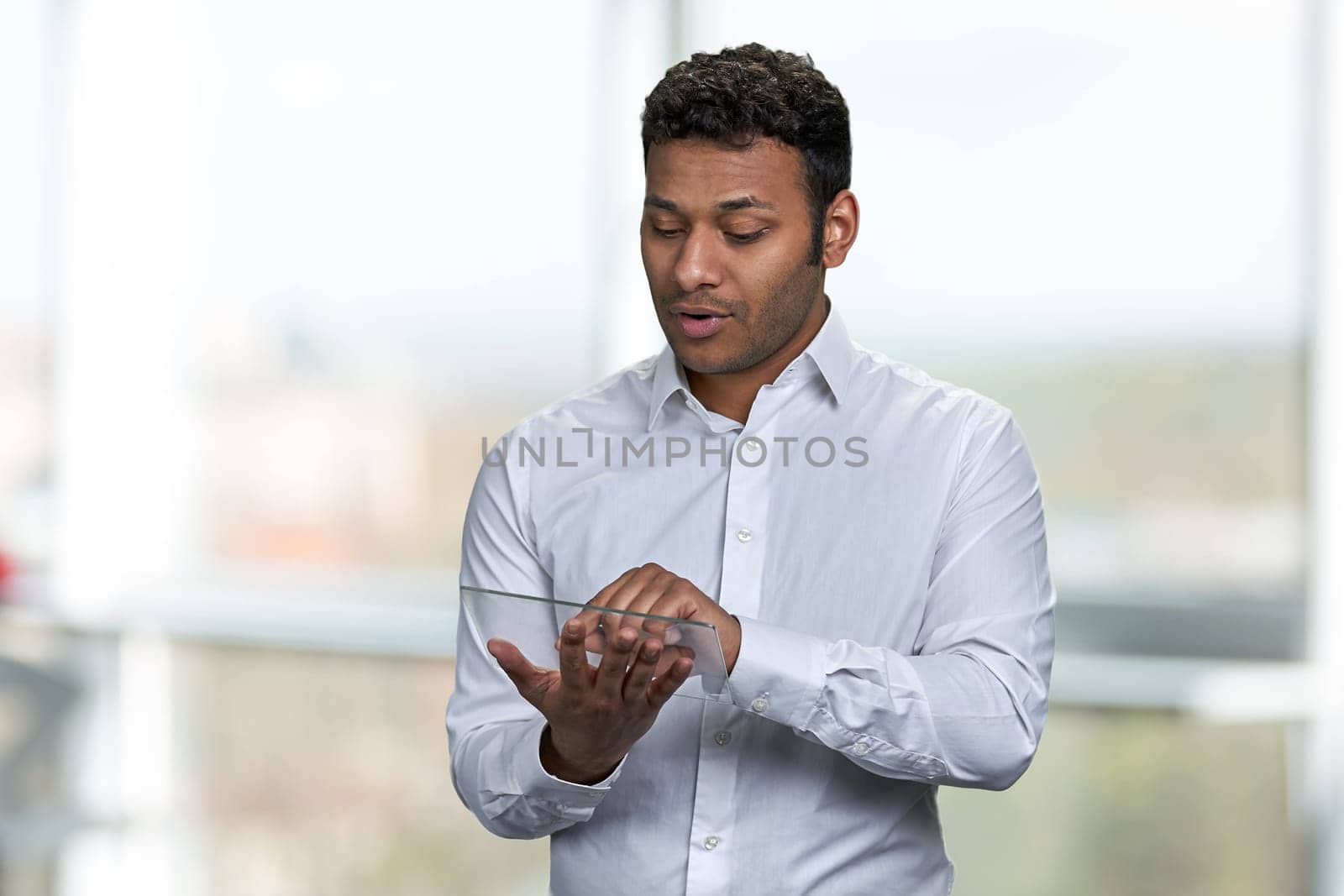 Young indian business speaker using transparent tablet pc. Blur interior background.