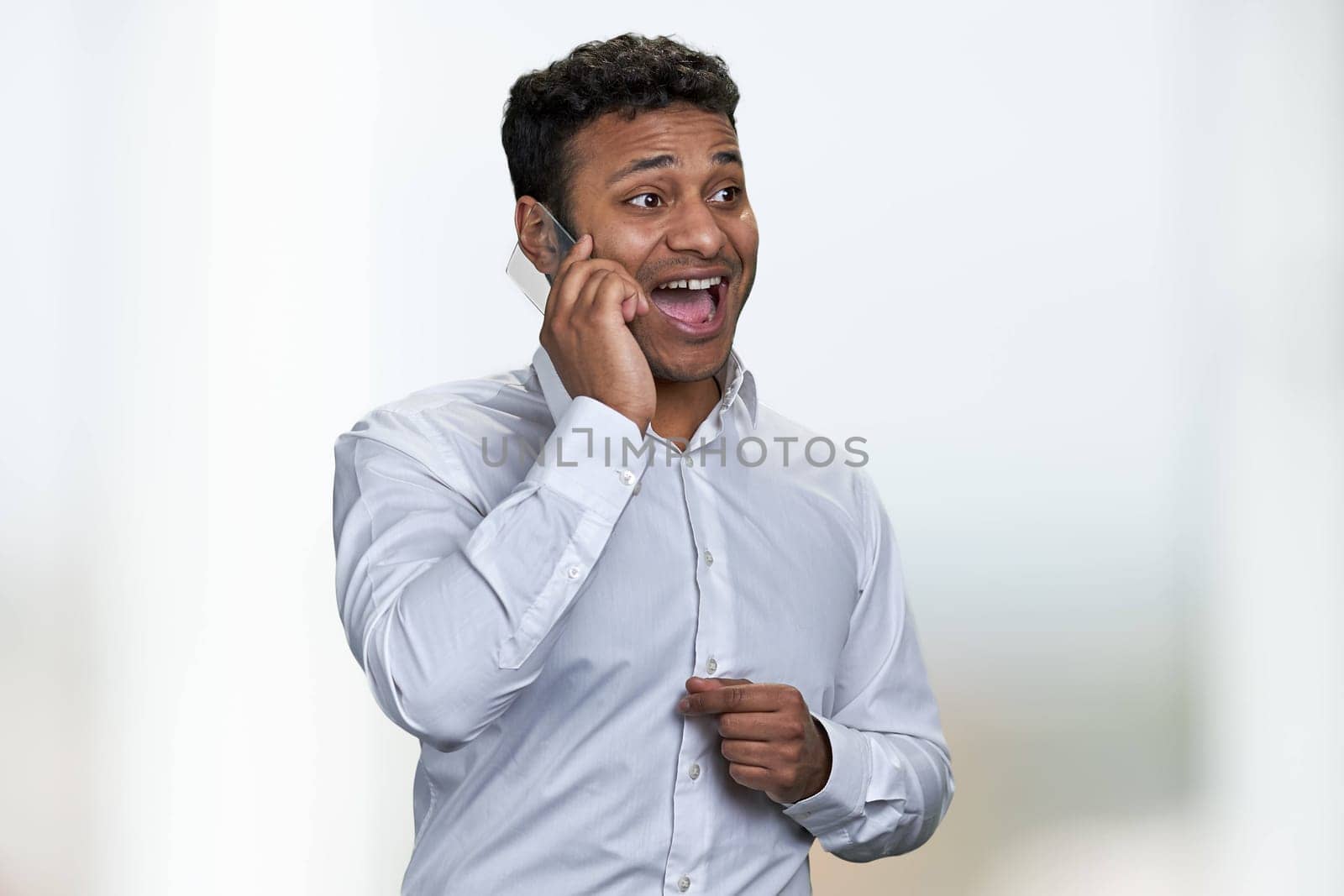 Overjoyed indian businessman talking on transparent phone against blurred background. People, business, modern technology and positive emotions.