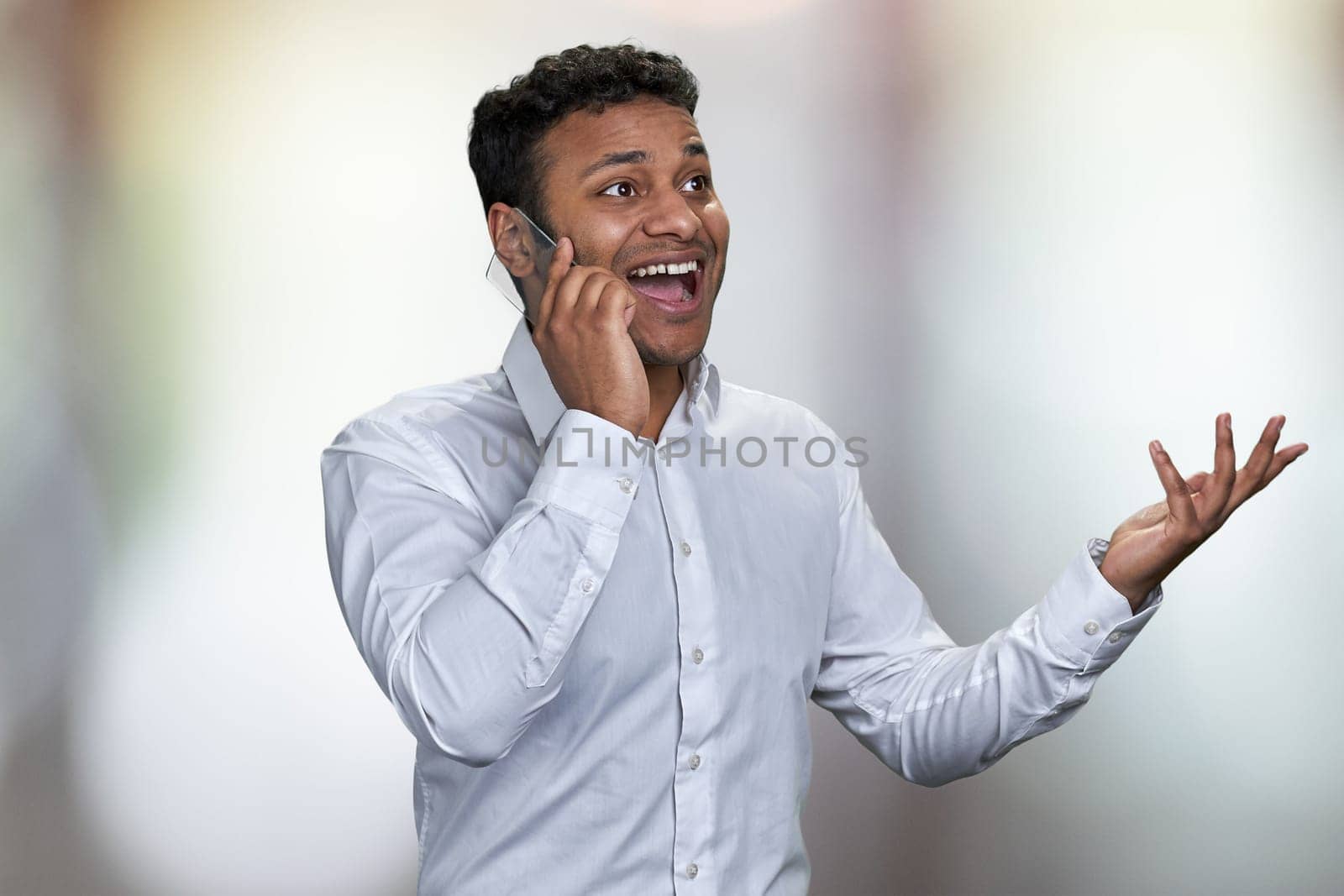 Portrait of young excited business man using futuristic mobile phone. Happy surprised man in white shirt talking on glass phone on abstract bokeh background.