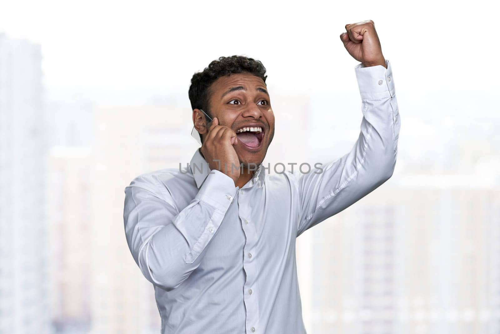 Young businessman talking on transparent phone and celebrating achievement with hand gesture. Business success concept.