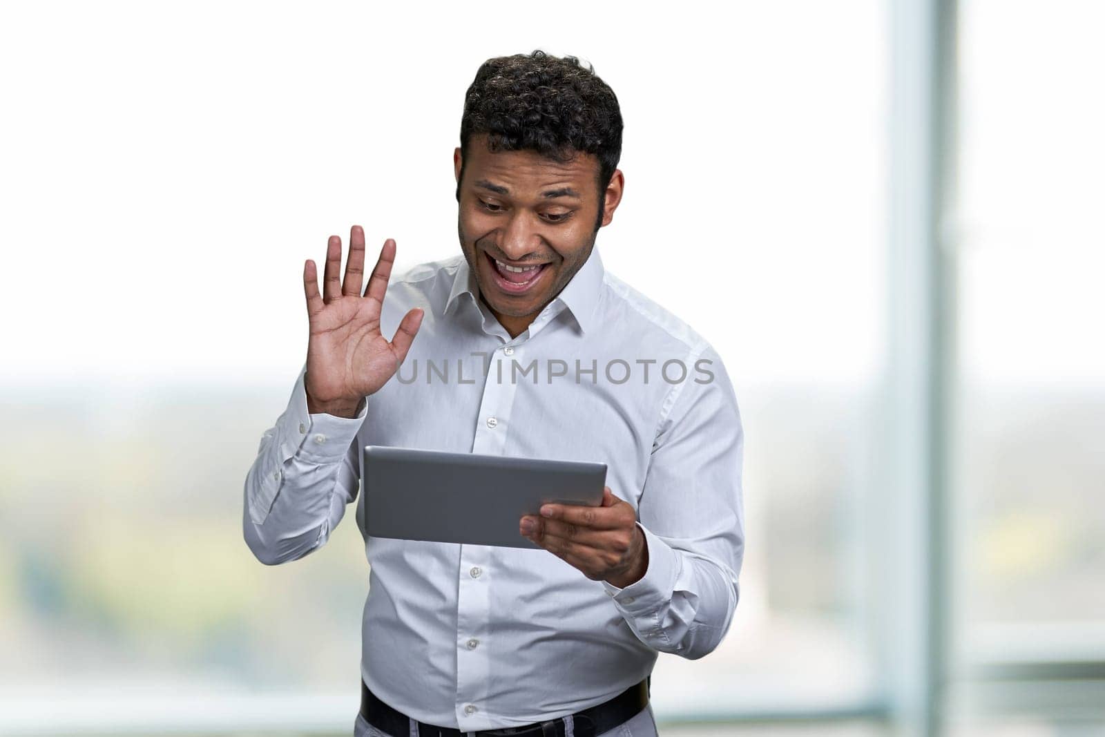 Cheerful african-american businessman making video call with digital tablet. Handsome man waving with hand while talking via internet.