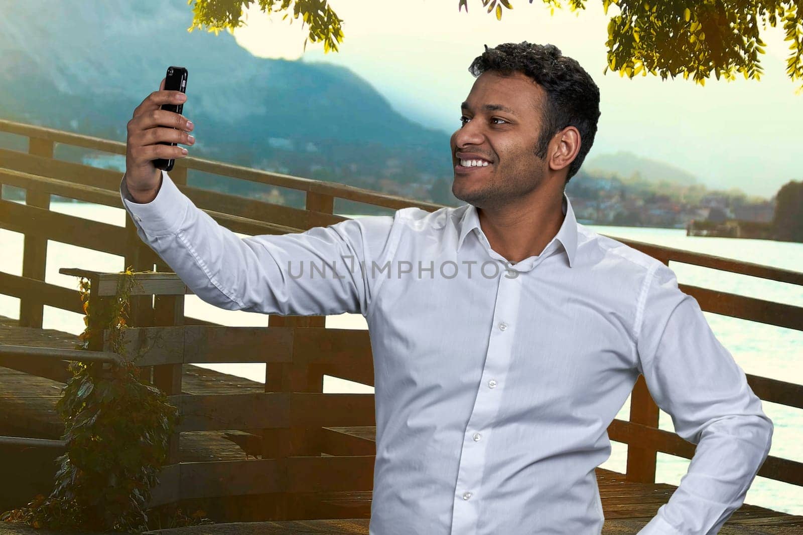 Smiling indian businessman taking selfie on his phone outdoors. People, technology and tourism concept.