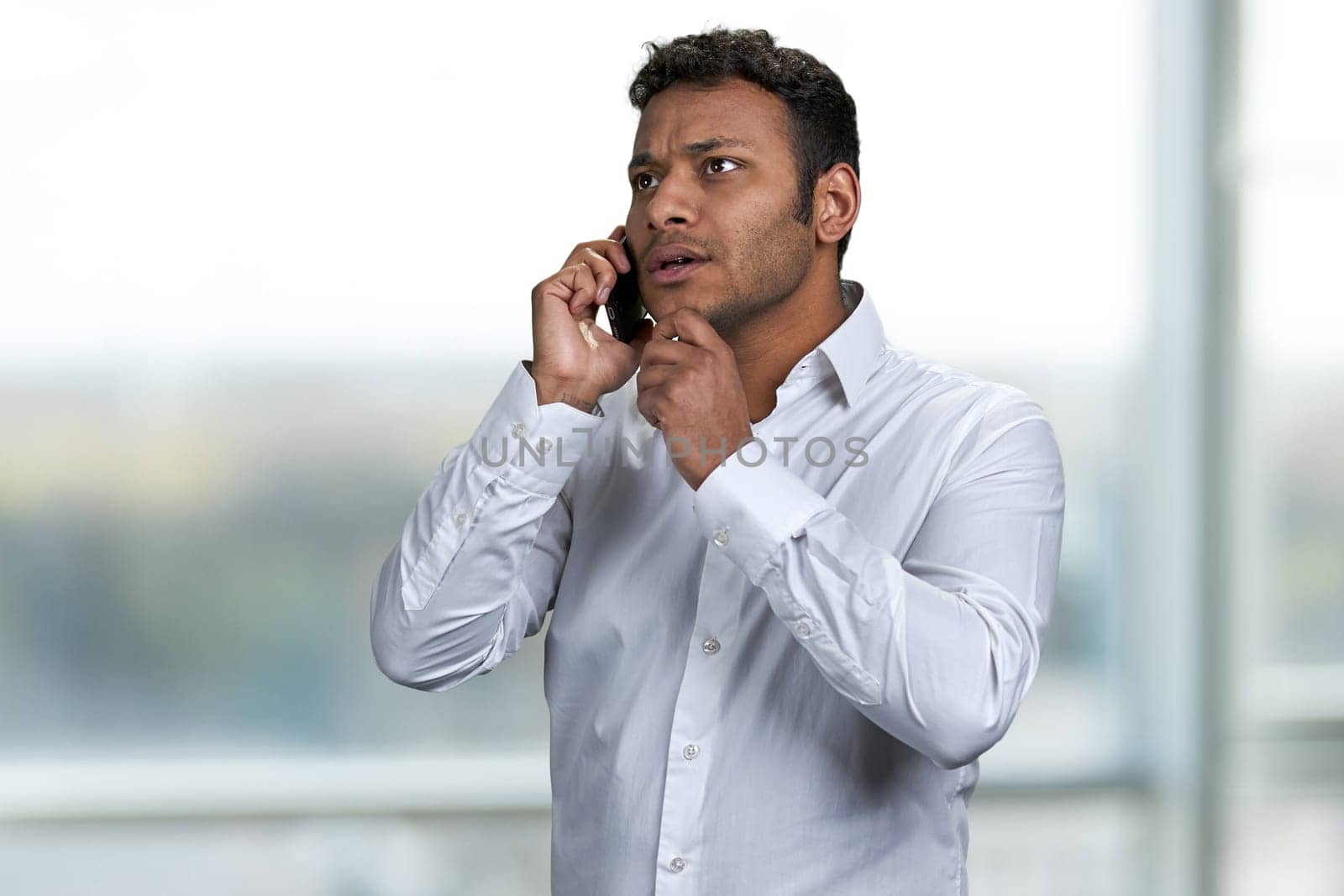 Serious handsome businessman talking on mobile phone with client. Blur window in the background.