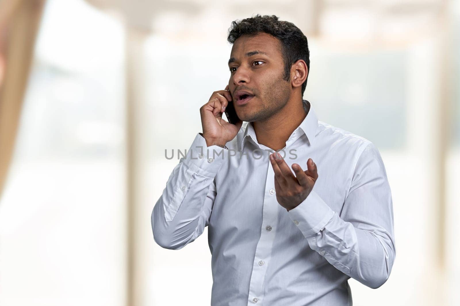 Serious young businessman talking to someone on mobile phone. Blur interior background.