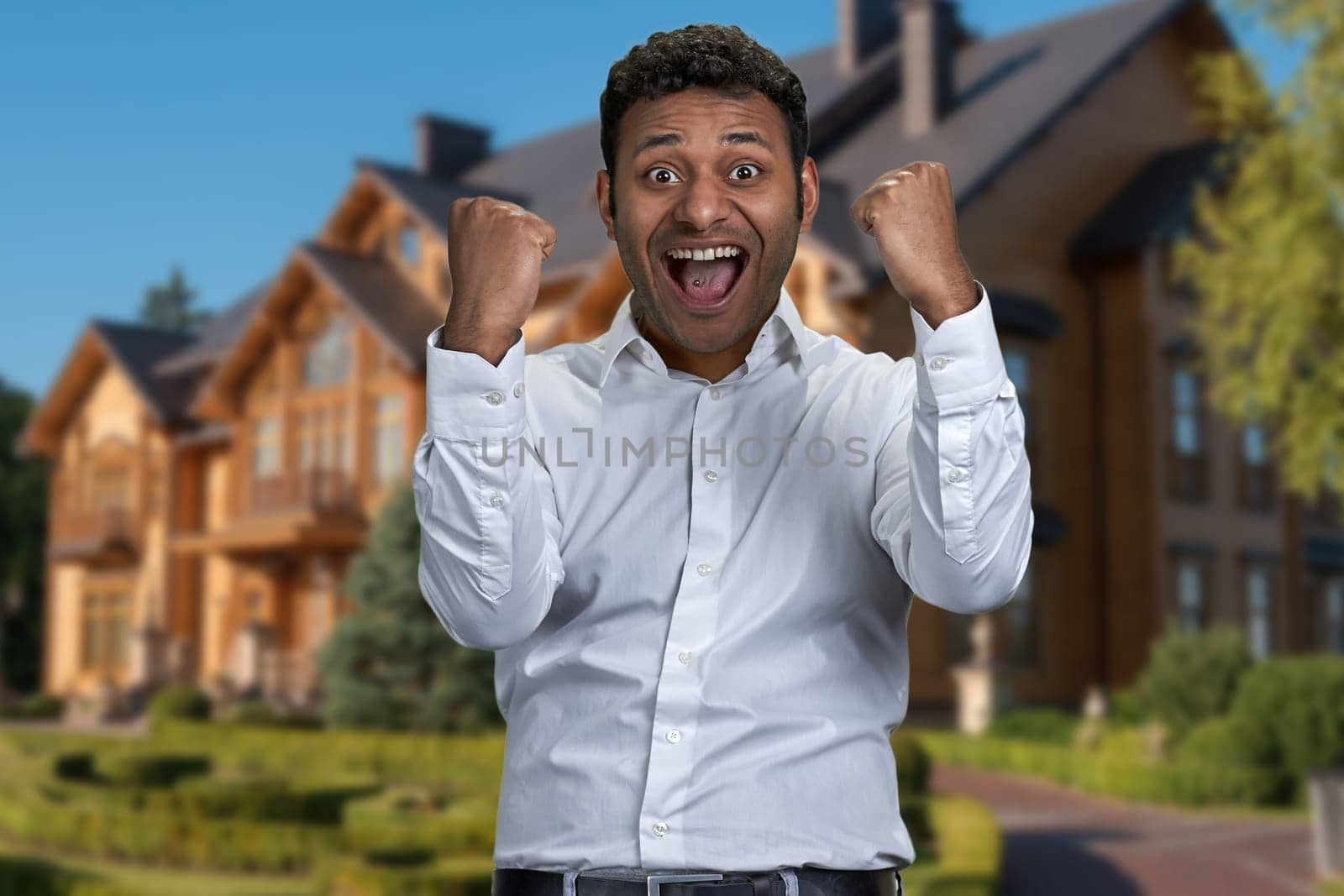 Overjoyed young man clenched his fists standing outdoors. Goal achievement concept.