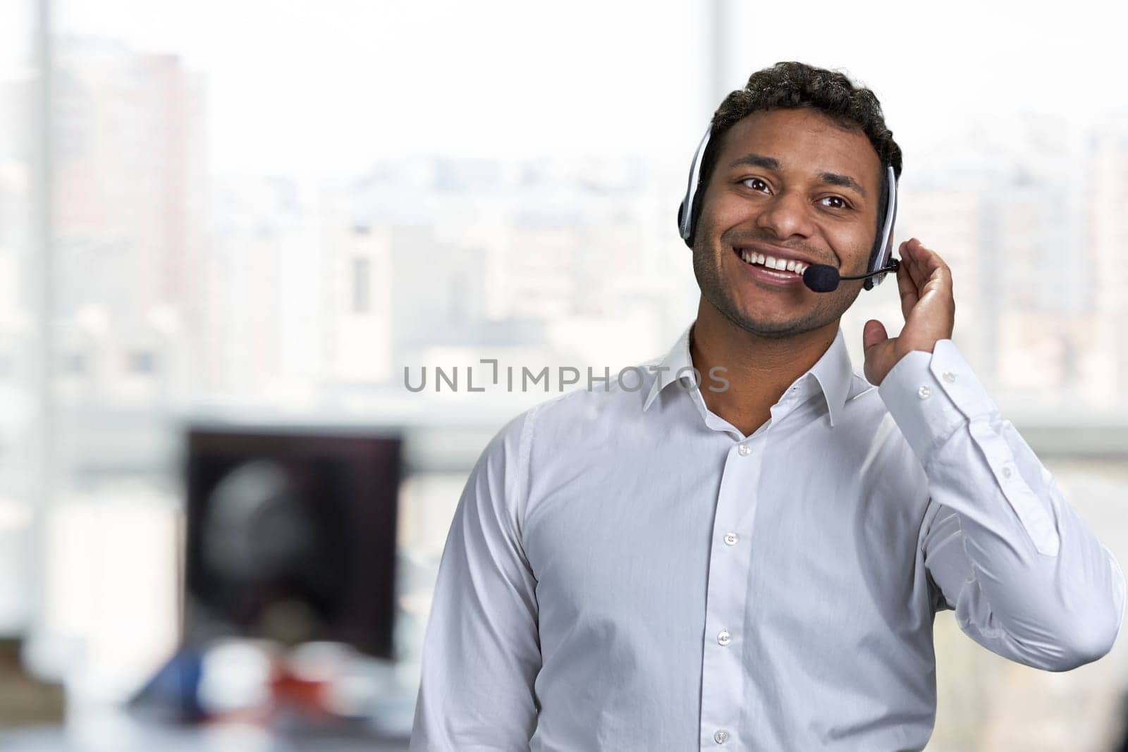 Smiling male call center agent talking to customer. Call center operator at work. Blur office interior in the background.